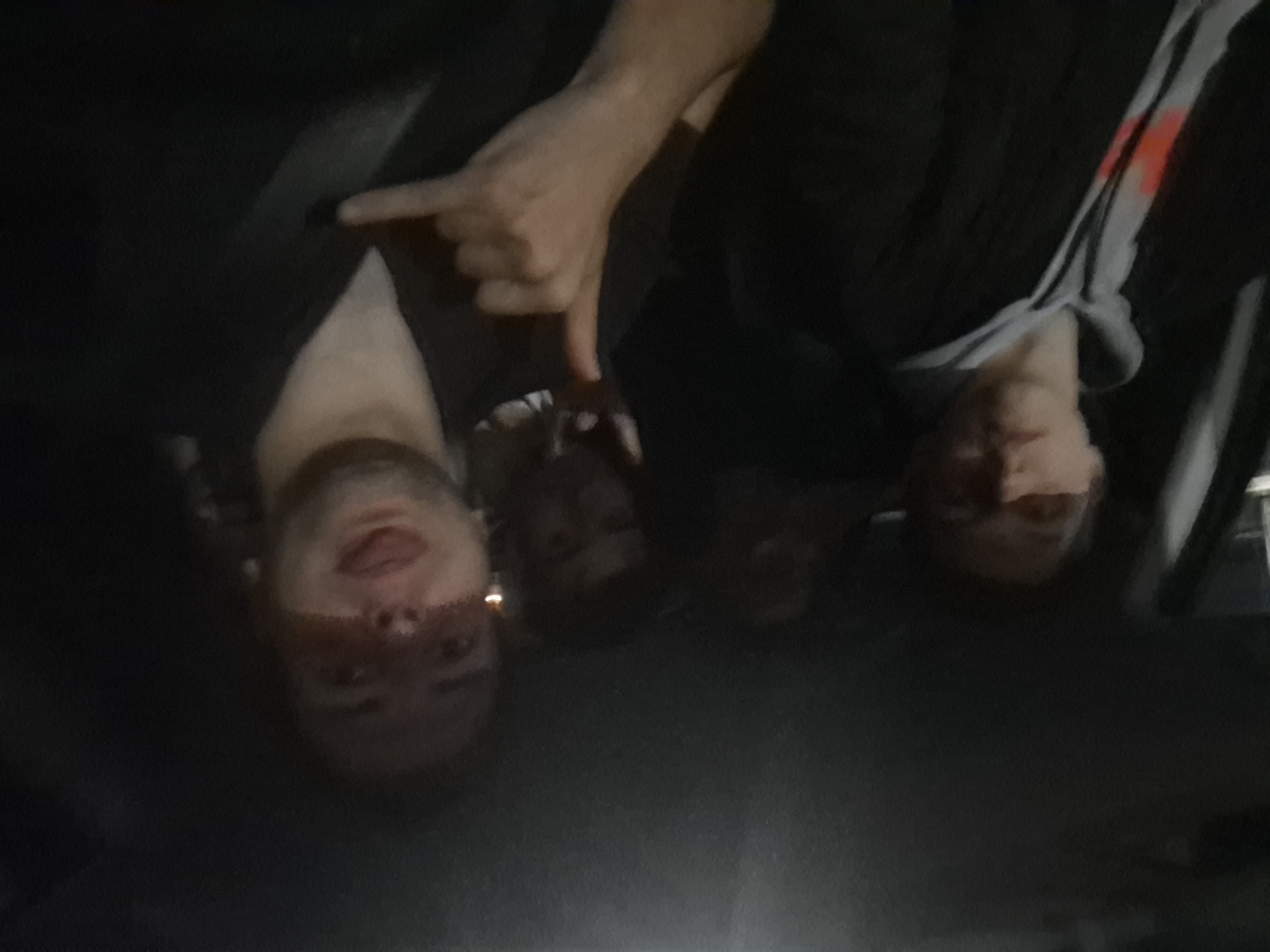 The image shows four individuals in what appears to be a car interior at night. The image is rotated 180 degrees. One person is pointing downwards with their index finger extended. The others are facing towards the camera. No identifiable location in Sofia, Bulgaria, is visible.