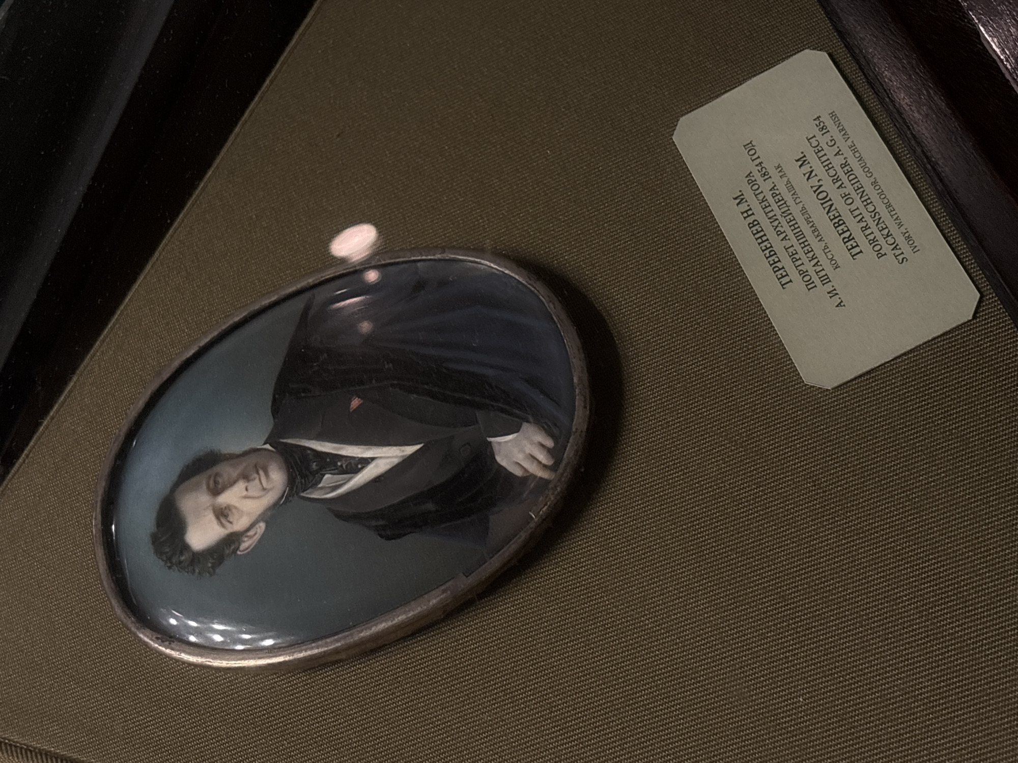 The image shows an oval portrait of a man in a dark suit, possibly from the mid-19th century, displayed next to a descriptive card. The card identifies the subject as N.M. Terebeniov, an architect, with the portrait being by A.G. Stackenschneider from 1854. The medium used is ivory, watercolor, gouache, and varnish. The card mentions Moscow.