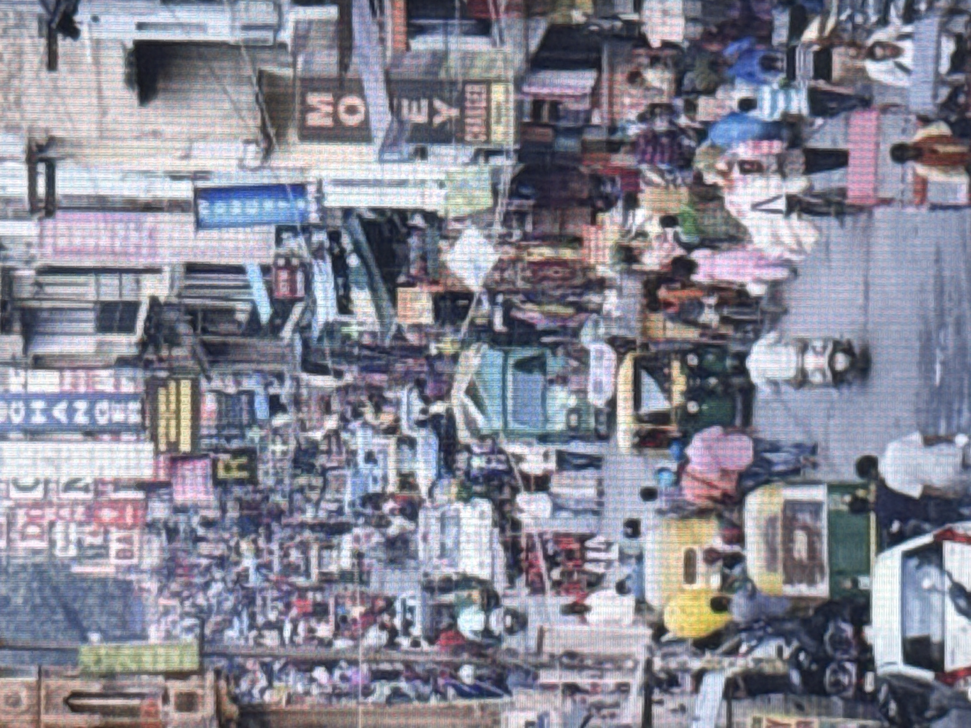 The image depicts a busy street scene in a city, likely in India, characterized by a high density of people, vehicles, and storefronts. The perspective is from an elevated viewpoint, looking down a narrow street lined with multi-story buildings. The street is filled with a variety of traffic, including cars, auto-rickshaws (tuk-tuks), scooters, and pedestrians. People are seen walking, riding vehicles, and interacting with each other. Storefronts are visible along both sides of the street, with various signs and awnings, suggesting commercial activity. The architecture appears to be traditional, with ornate detailing on some of the buildings. The overall atmosphere is one of bustling activity and a vibrant urban environment. Signs in English and what appears to be Hindi are visible, contributing to the sense of location. The image has a painterly quality due to its pixelated texture.