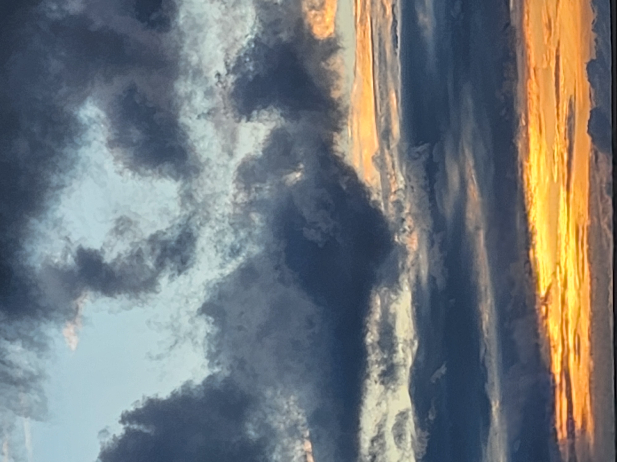 The image depicts a dramatic sky scene, characteristic of either sunrise or sunset, over Krasnogorskoye, Russia. The sky is dominated by textured, dark blue-grey clouds that stretch across the frame, contrasting with areas of bright, warm golden-orange light, particularly concentrated along the right side of the image. Interspersed among the darker cloud formations are patches of lighter blue sky and some white or light-grey clouds, illuminated by the sun's low angle.
The lighting creates a strong contrast between the brilliant, sunlit portions and the deep, shadowed parts of the clouds. No people, man-made objects, or visible text are present in the image, focusing entirely on the natural phenomenon. The various crops provided serve to highlight different sections of these cloud formations and the interplay of light and shadow, emphasizing the rich color palette and dynamic cloud structures without introducing new subjects or details. The overall impression is one of natural beauty and an atmospheric display of light.
