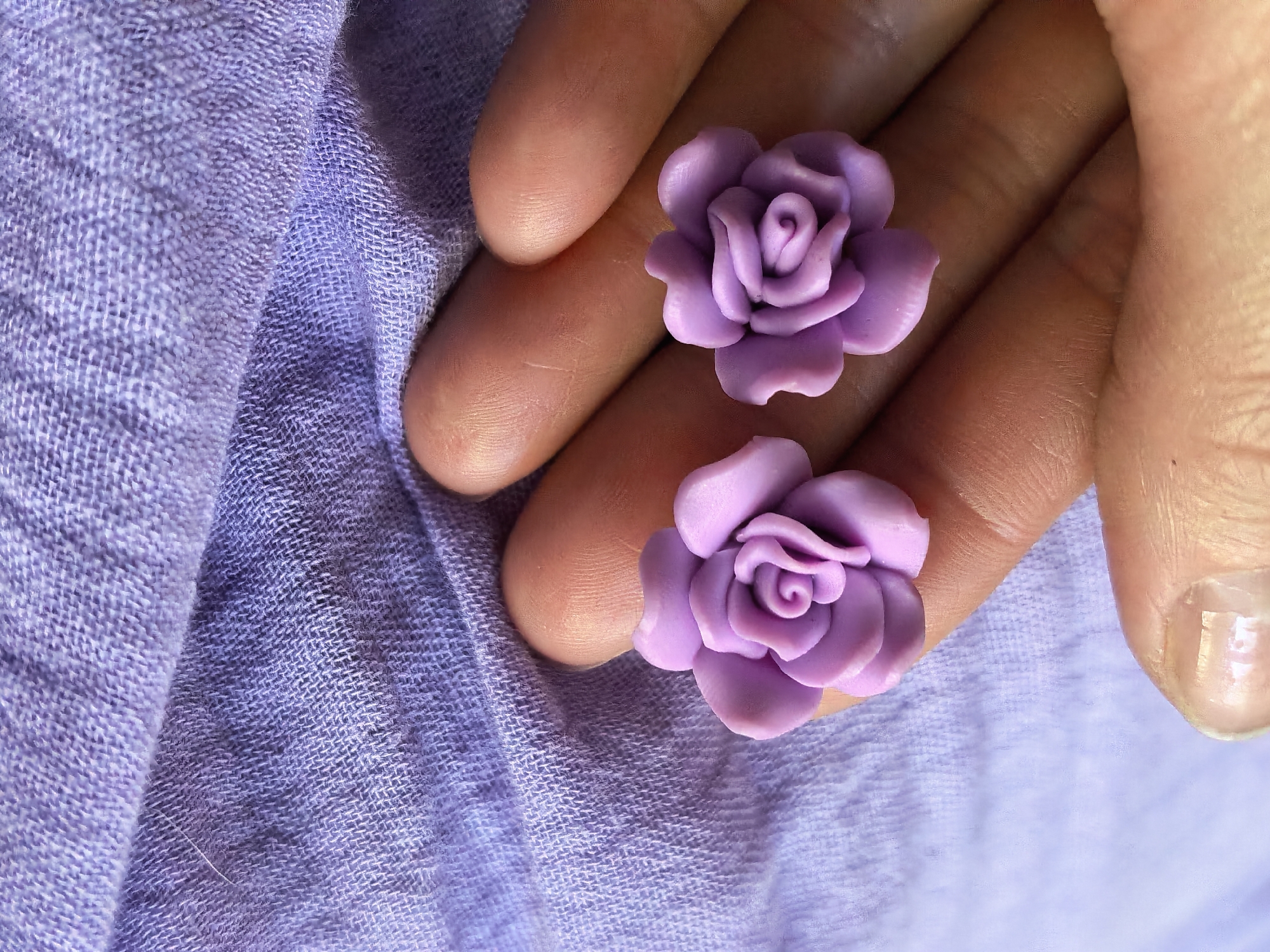 The image shows two lavender-colored rose-shaped objects resting on a person's hand. The hand is positioned over a light purple, textured fabric. No specific information indicates the city of Sterlitamak, Russia.
