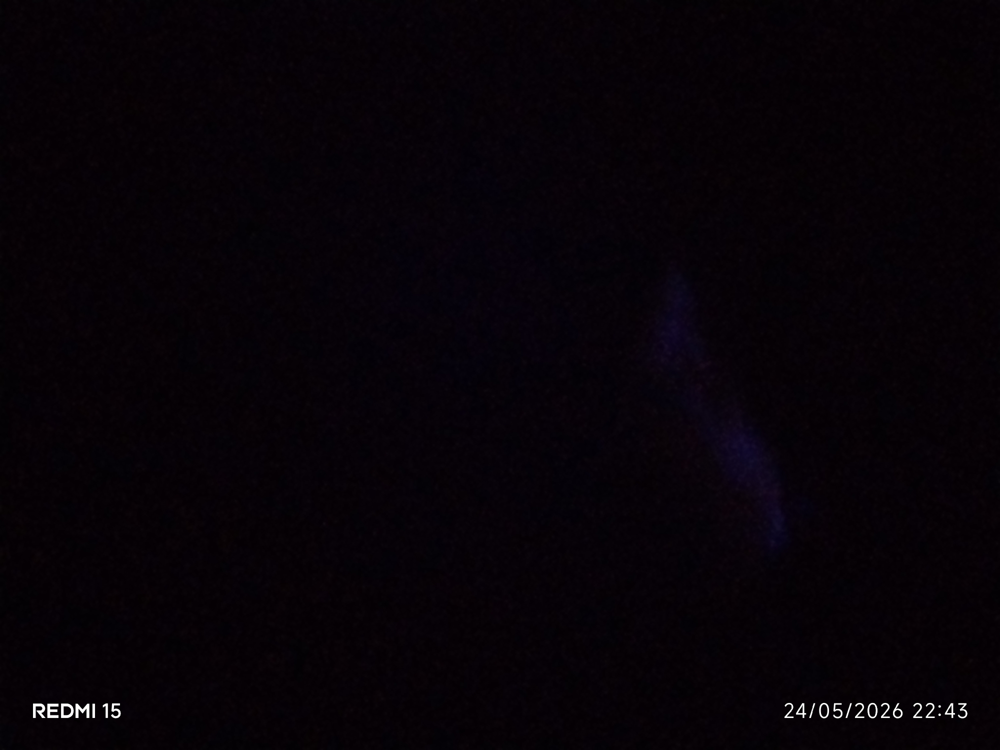 The image is a dark, low-light photo, likely taken at night. The only visible detail is a faint, elongated area of blueish light in the right center of the frame. In the lower left corner of the image, "REDMI 15" is visible. In the lower right corner, the timestamp "24/05/2026 22:43" is displayed. There is no discernible information about the location in Narayi, Nigeria, or any subjects, objects, actions, or interactions.