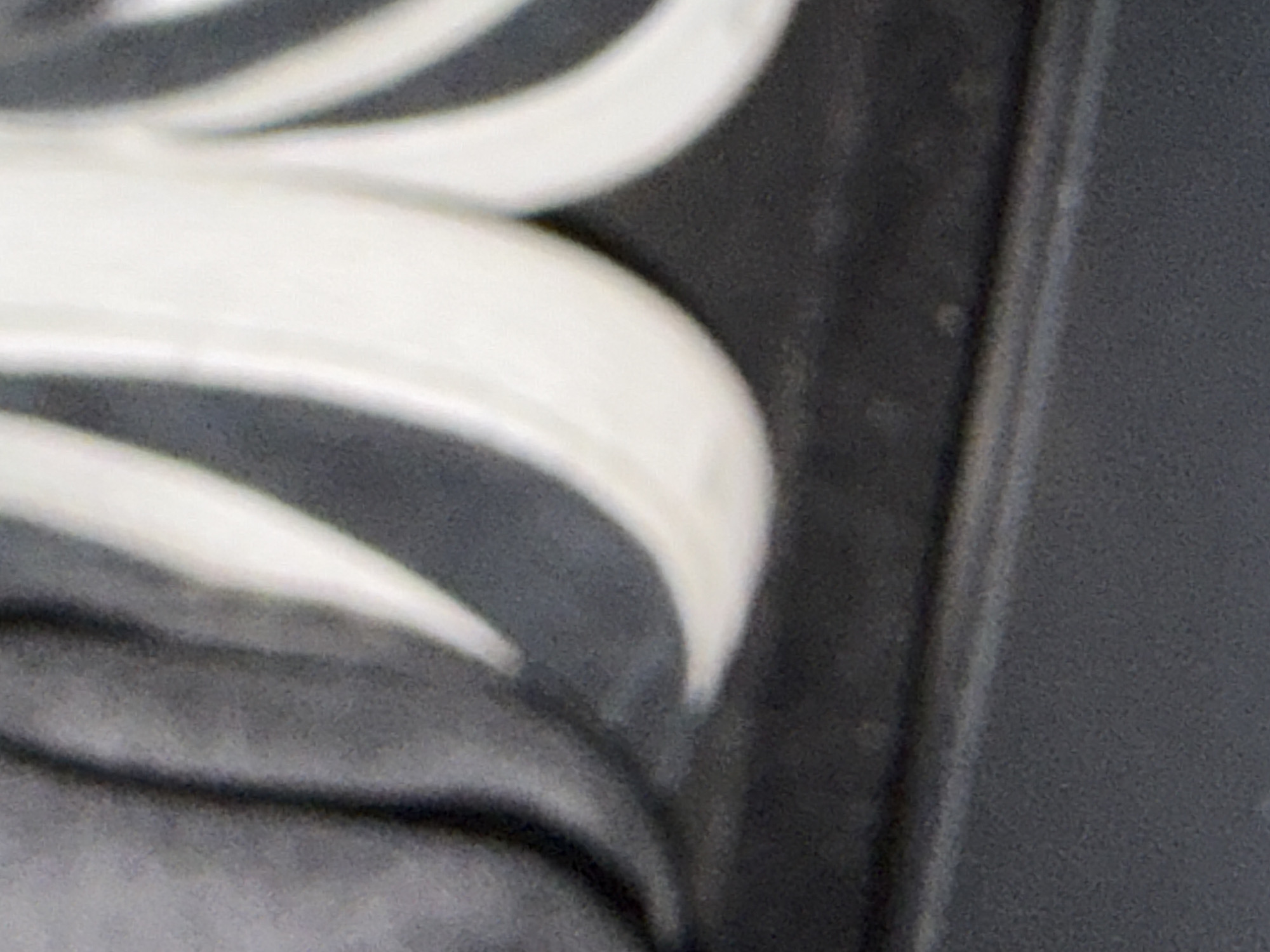 The image is a close-up, abstract shot of a textured surface with dark gray and white elements. The texture appears to be a stylized decorative pattern, possibly carved or molded, with rounded, flowing shapes. The lighting creates shadows and highlights that emphasize the depth and form of the material. The lower portion of the image shows a flatter, matte dark gray surface, which could be a base or surrounding area. The image does not contain any discernible elements that would allow for identification of a specific city, location, or any environmental context such as Ödsmål, Sweden.
