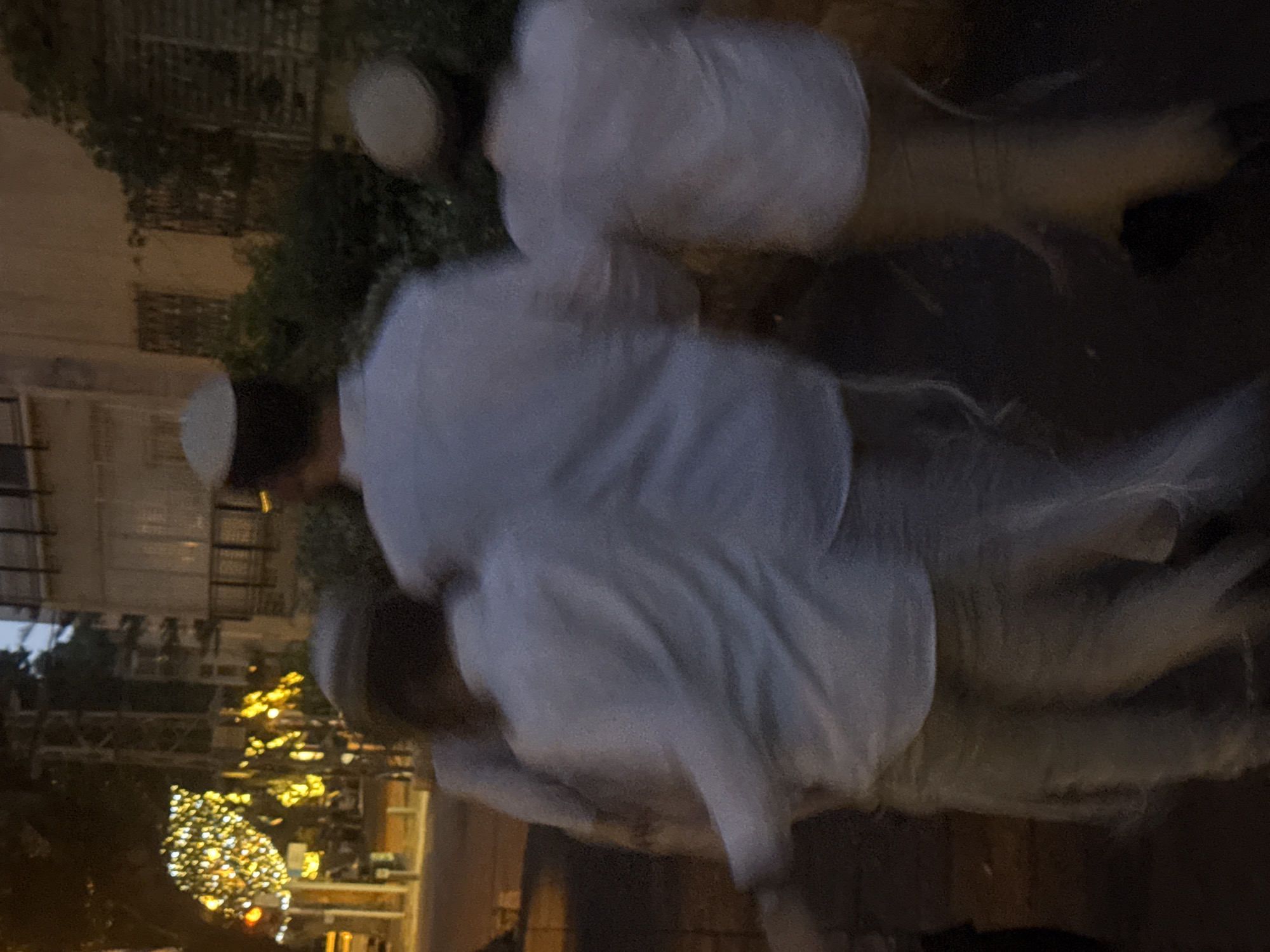 The image shows three Orthodox Jewish men in Ramat Gan, Israel. They are wearing white shirts and kippahs. They appear to be walking outdoors at night. There is a Christmas tree in the background. There are buildings on the left of the frame.