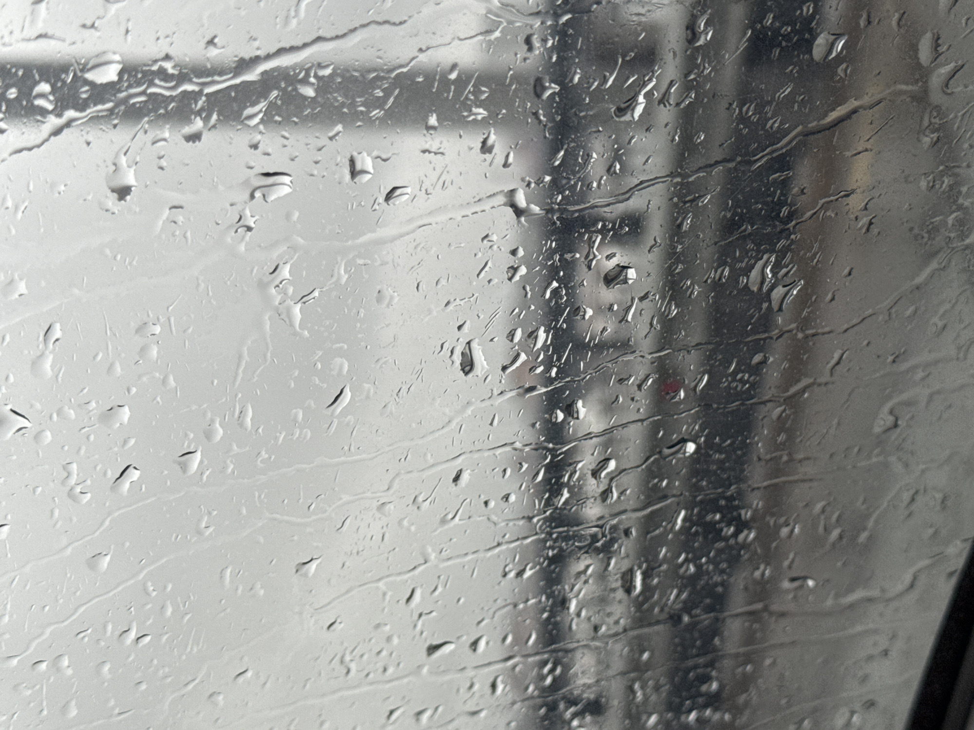 Raindrops cover a window, obscuring the view of what appears to be a car wash structure. Reflections of machinery and the structure are visible through the water. The location of the image is unknown and there is nothing to indicate that it is taken in Perm, Russia.