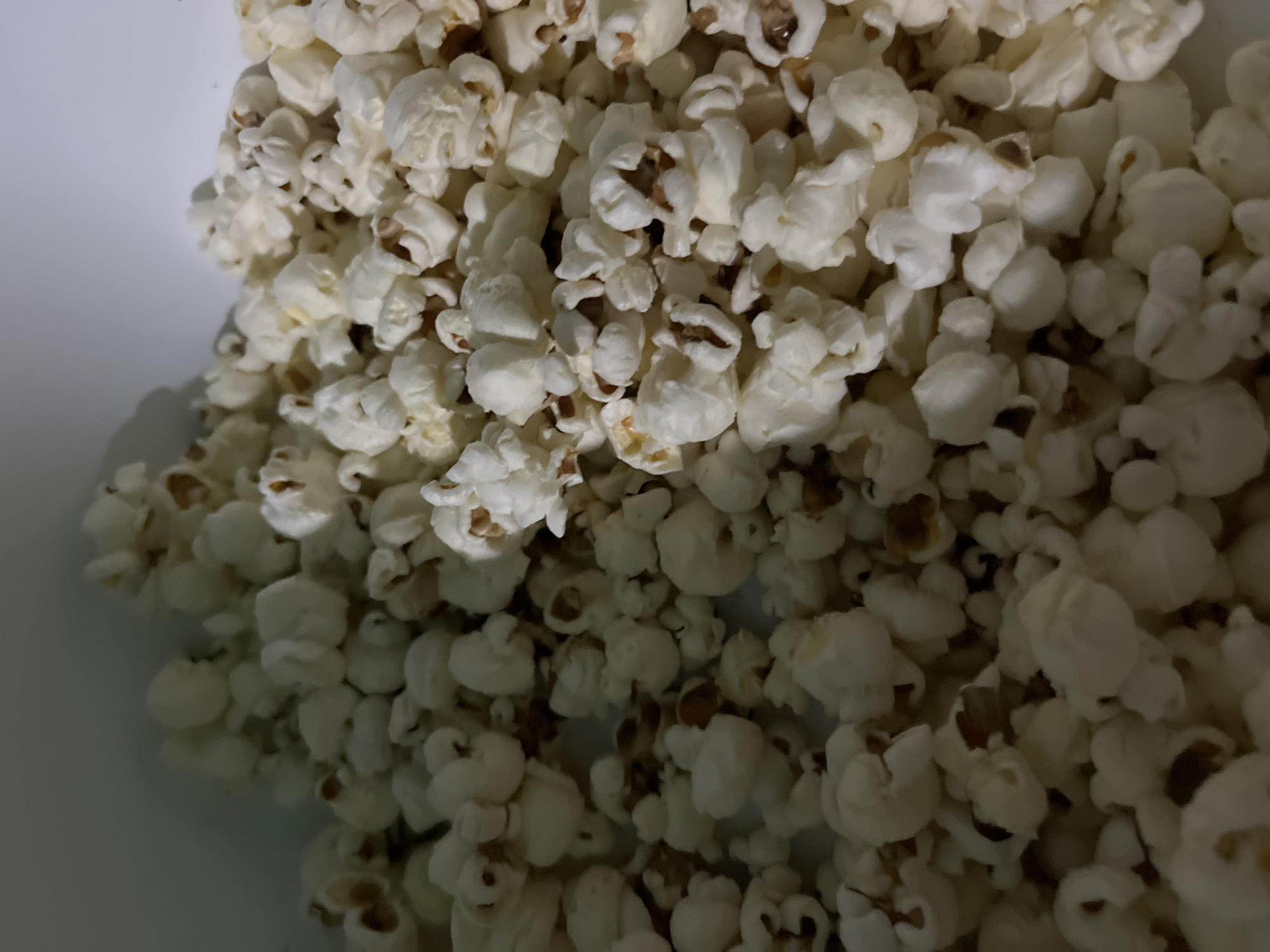 The image shows a close-up of a large pile of white popcorn. Some kernels have dark brown tips. The popcorn appears to be contained within a white bowl or container, as the edges of the container are visible. There is no indication in the image that this scene is located in Juan Griego, Venezuela. No people, actions, or interactions are depicted.