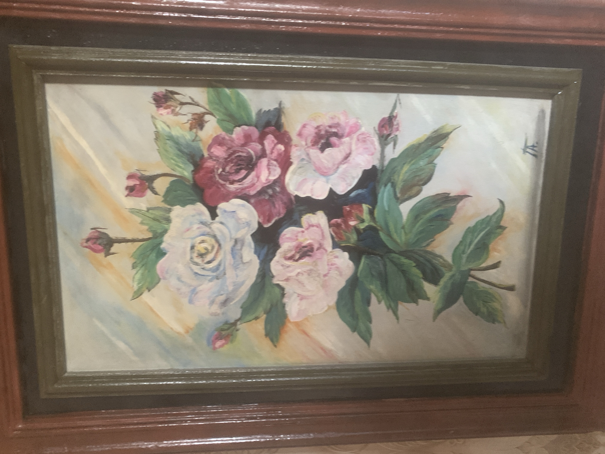 The image displays a framed painting of a floral arrangement featuring roses and leaves against a pastel background. The painting is housed in a wooden frame with multiple layers of molding. The overall impression is that of a decorative art piece. The provided context indicates the painting is located in the city of Gyumri, Armenia, suggesting it might be part of a collection in a museum, gallery, or private residence within the city. No specific details about the city of Gyumri or its landmarks are visible in the image itself.
