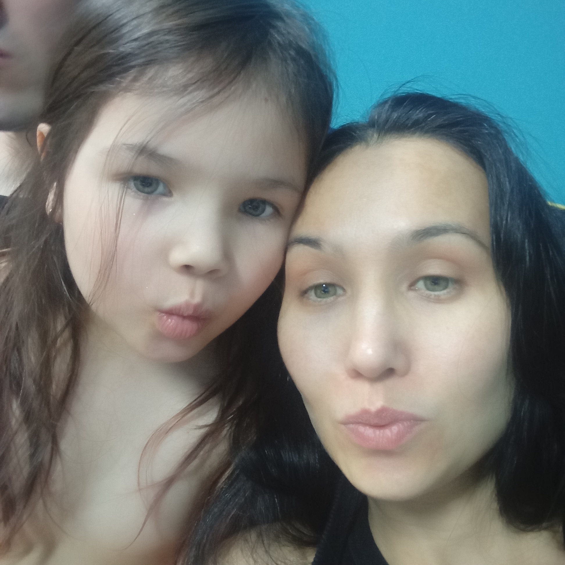 A selfie of a woman and a child with light skin and dark hair, both making a pursed lips face. The background is a blue wall. The photo's location in Pervomaysky, Russia, is not discernible from the visual information provided.