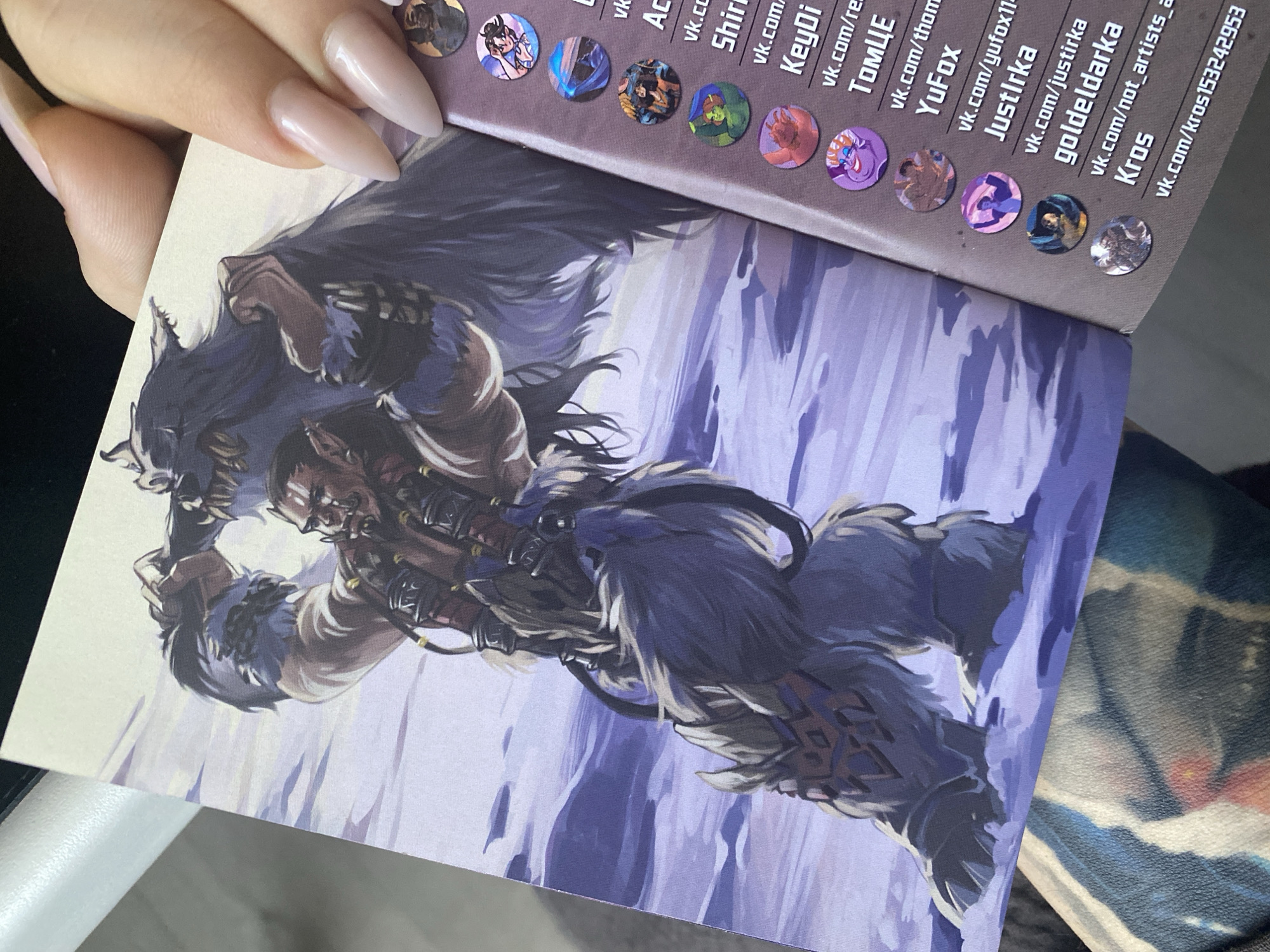 A hand with long, almond-shaped fingernails holds open a booklet or pamphlet. The inside features a stylized illustration of a muscular, hirsute figure with lupine features and wearing fur garments, posed against a wintry, light blue backdrop. The facing page lists names in a column, accompanied by small, circular images, and website links beginning with "vk.com," the Russian social media platform VKontakte. The final name is "Kros vk.com/kros153242953".