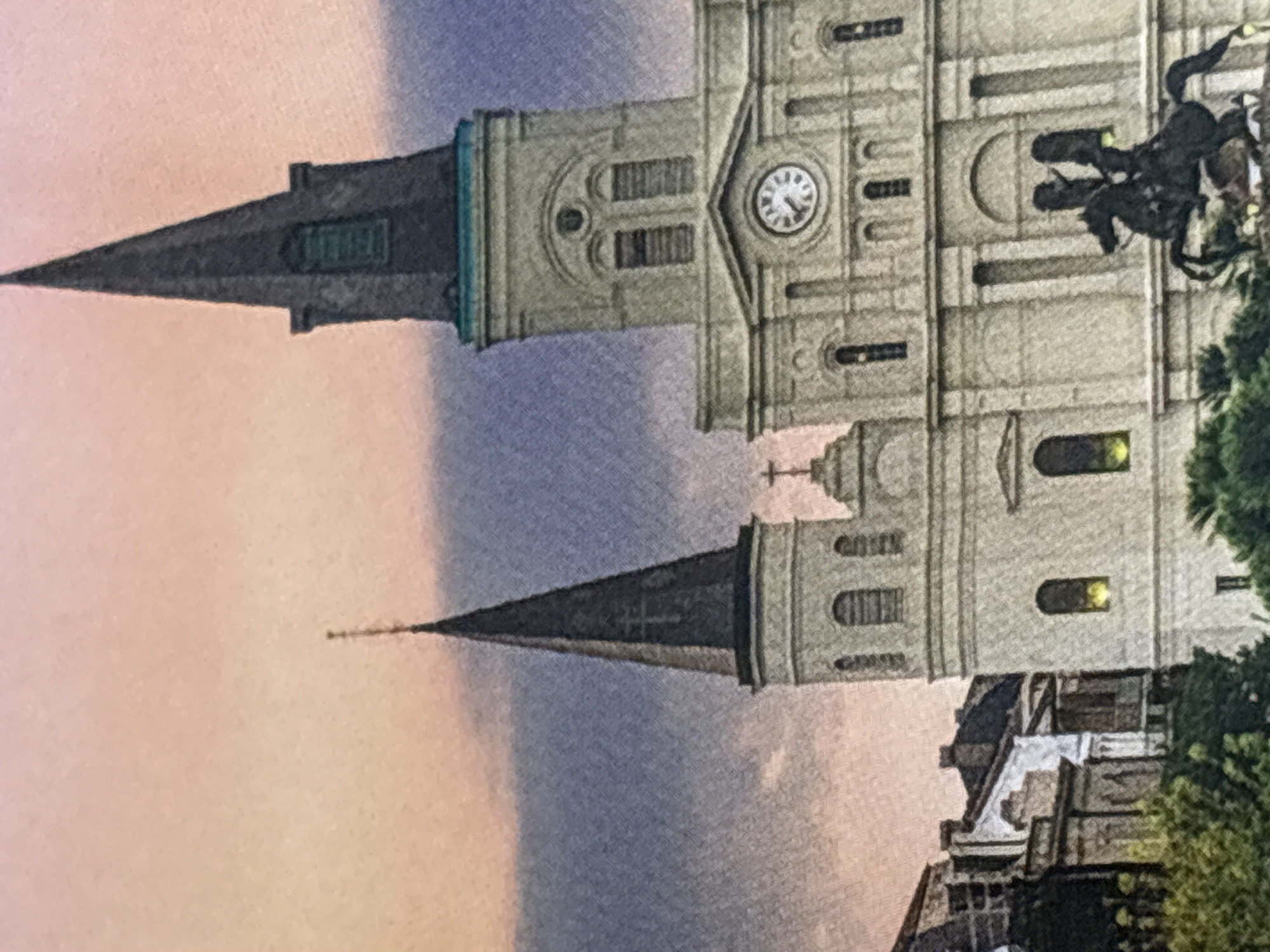 The image shows a close-up view of the facade of St. Louis Cathedral in New Orleans, Louisiana, USA. The cathedral's distinctive spires and architectural details are visible against a twilight sky with hues of pink and purple. A clock face is prominently displayed on the central tower, and an equestrian statue is in the foreground, partially obscured by greenery. The surrounding buildings and trees suggest an urban setting. The image is a still photograph, with no people or animals actively engaged in any actions. The description of Chelmsford, United Kingdom is not applicable as the image depicts a landmark in New Orleans.