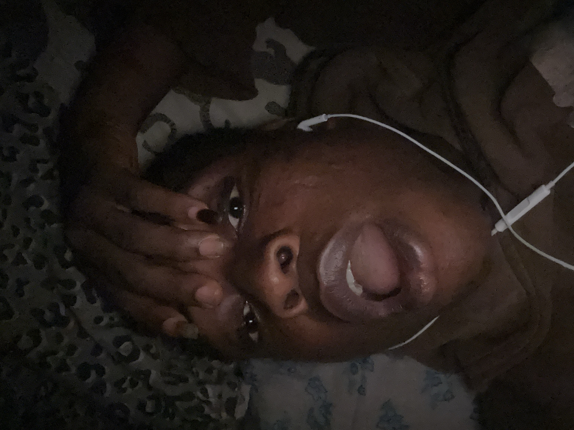 A person lies on a patterned bed with an open mouth and headphones. The location is unknown.