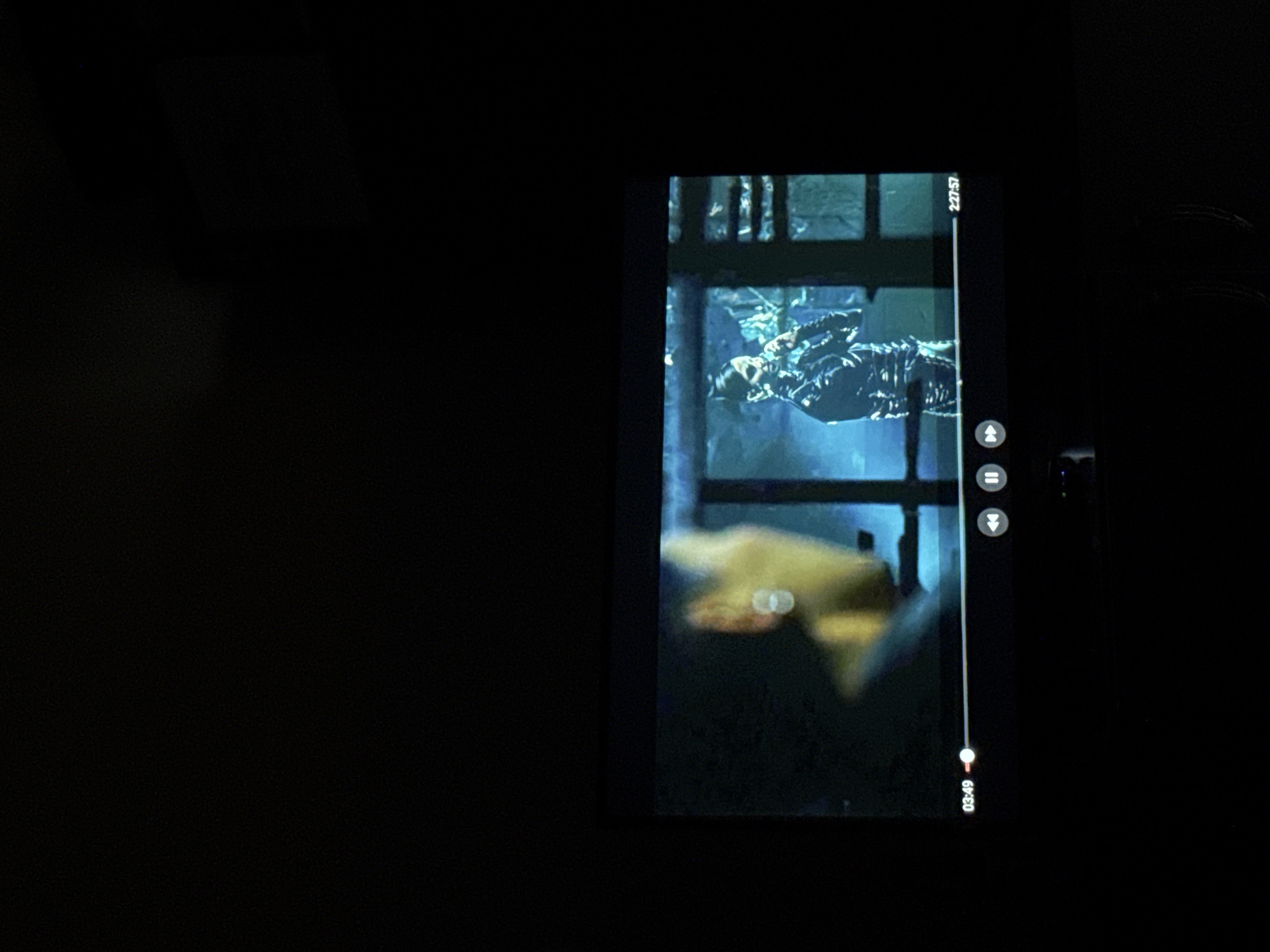 A photograph shows a small screen, possibly of a phone or tablet, displaying a scene from a video. The video appears to be set in a dimly lit environment and features a person wearing a dark, textured garment, positioned behind what seems to be a window or barred structure. The overall color tone is blueish, contributing to a somber mood. The scene on the screen seems to have a gritty texture.
The image does not contain any information to identify any location in Sofia, Bulgaria.