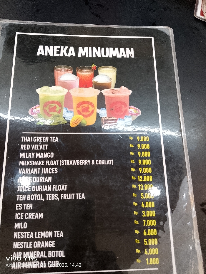 The image shows a menu of drinks displayed on a black background with a black frame. The title of the menu is "ANEKA MINUMAN." The menu features 13 different types of drinks, with prices listed in Indonesian Rupiah (Rp.). The drinks include: Thai green tea, red velvet, milky mango, milkshake float (strawberry & coklat), variant juices, juice durian, juice durian float, teh botol, tebs, fruit tea, es teh, ice cream, milo, nestea lemon tea, nestle orange, air mineral botol, and air mineral cup. There are five clear plastic cups filled with different colored beverages in the upper left corner of the menu. The location of the menu is inferred to be Patrol, Indonesia, using the coordinates -6.318 latitude and 107.986 longitude.
