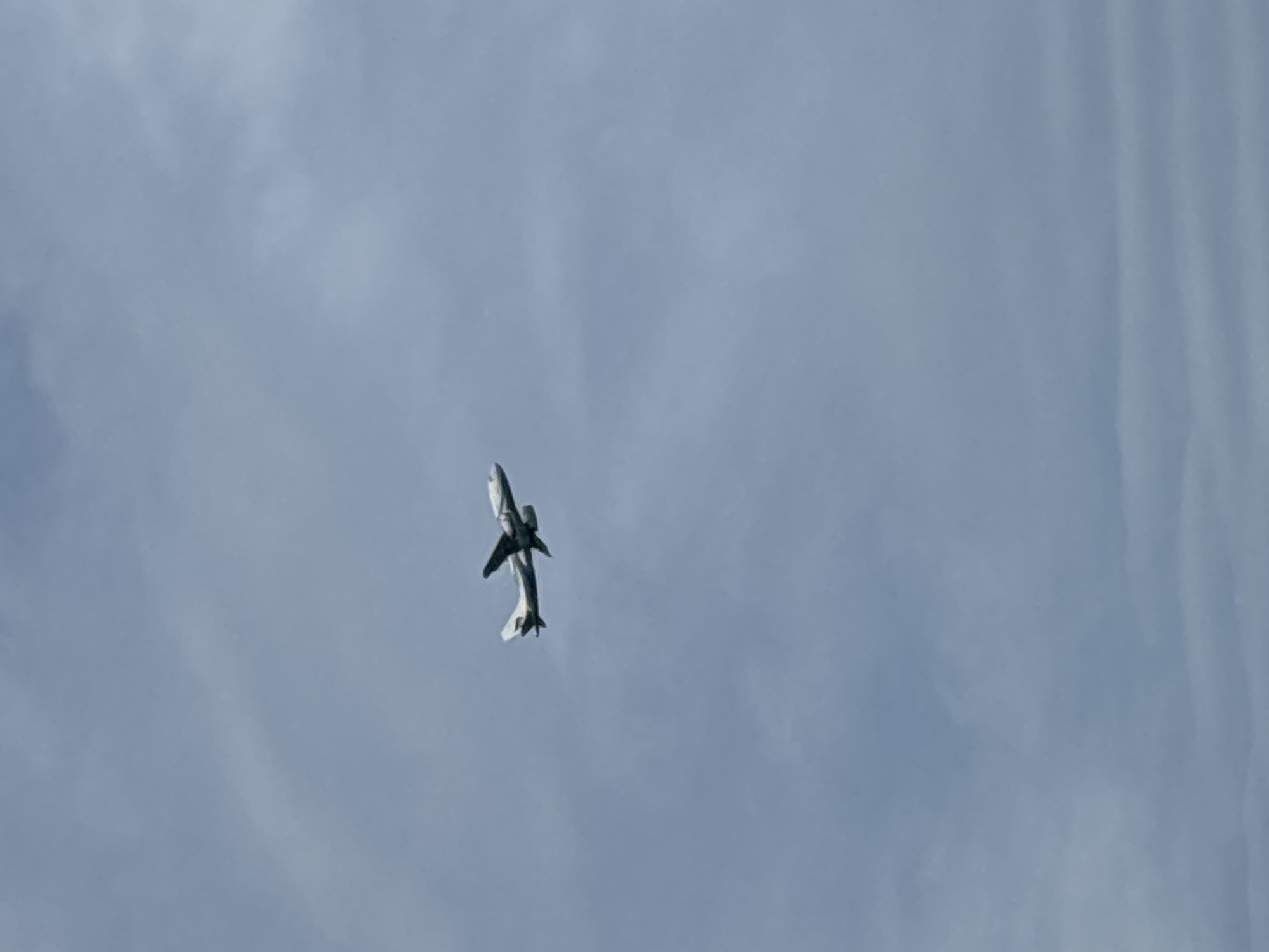 The image shows an airplane flying in the sky. The sky appears overcast. The plane is white and silver with dark wing accents. The location, Baan Chaweng, Thailand, is not discernable from the image.