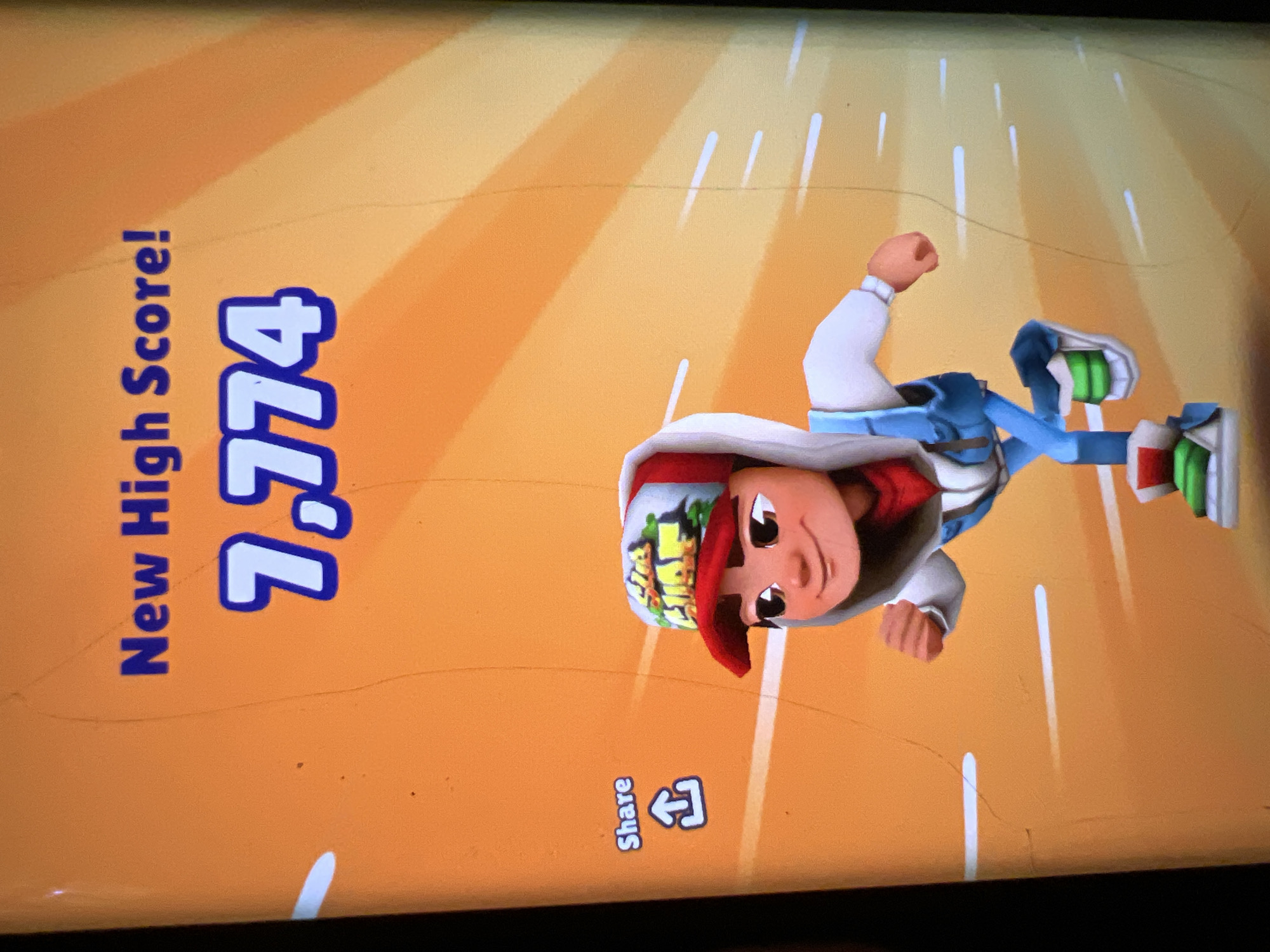 The image displays a screen capture from the mobile game "Subway Surfers" showing a "New High Score!" of 7,774. In the foreground, the game's character, a young boy with a red and white cap, is depicted running. To the left of the character, there is a "Share" button with an upward-pointing arrow icon. The background is a bright orange with radiating yellow lines, simulating a sense of speed. There are no discernible elements in the image that would place it in Lagos, Nigeria.