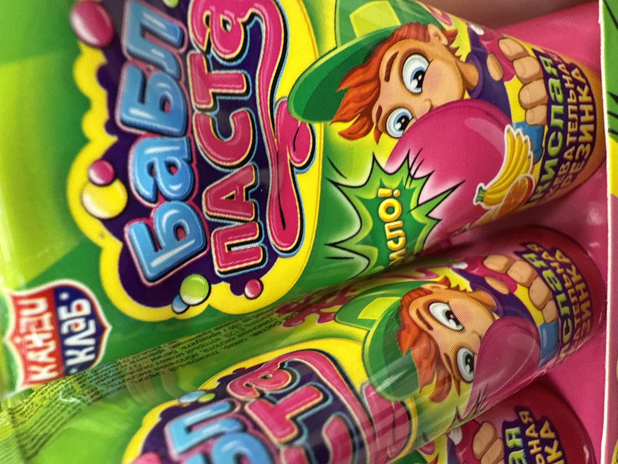 The image shows a close-up of brightly colored candy tubes, labeled "Babi Paste." The tubes feature cartoonish characters and stylized text in Russian. The text also includes "Kandi Klub." Another part of the text reads "acid."