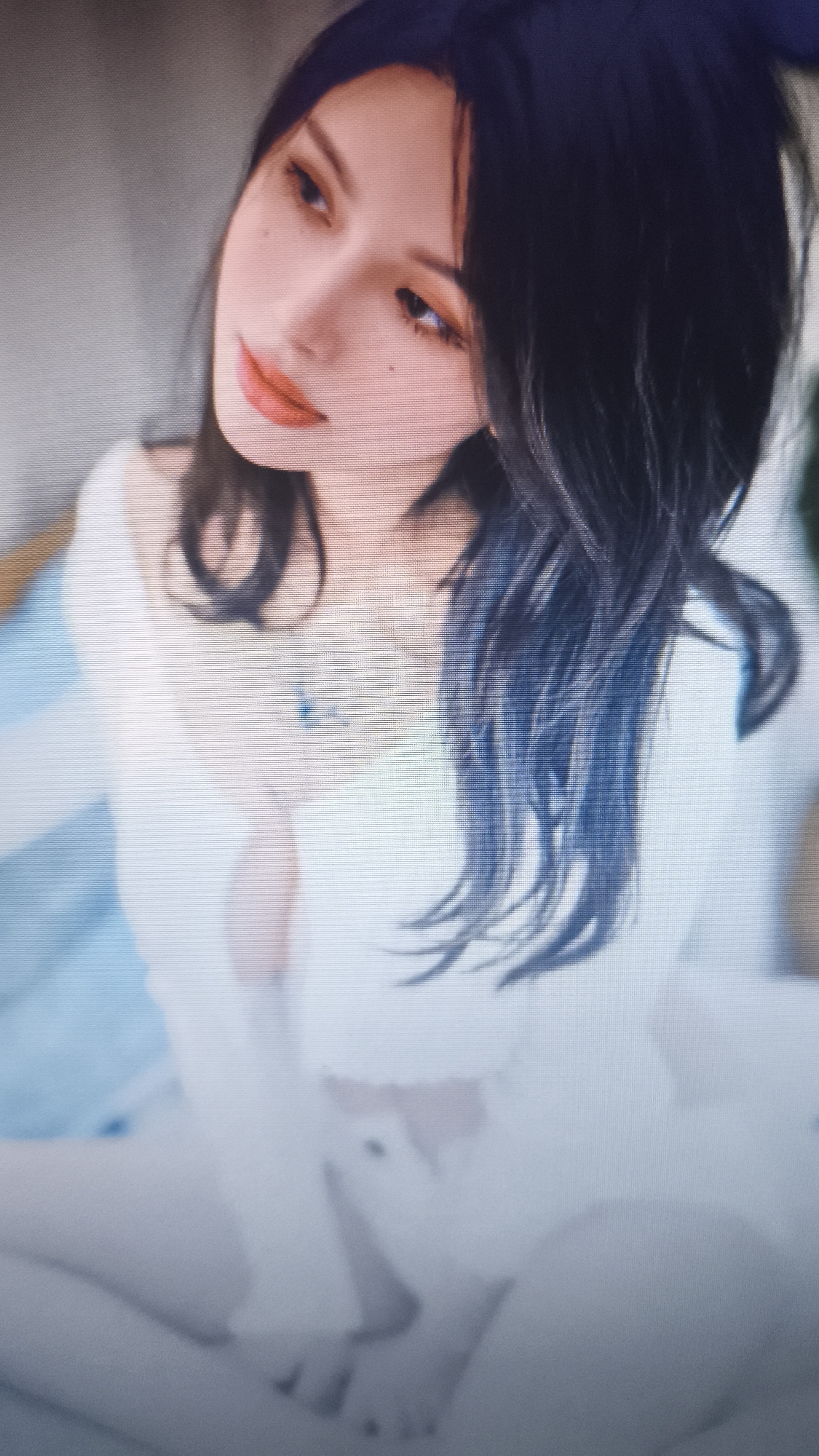 A person with long, dark hair is looking to their left in a portrait. The person has fair skin and orange lipstick, and is wearing a white top. A small tattoo is visible on their chest. Their hands are crossed in their lap and blurred. The location in the city of Nowy Tomyśl, Poland, is unknown.