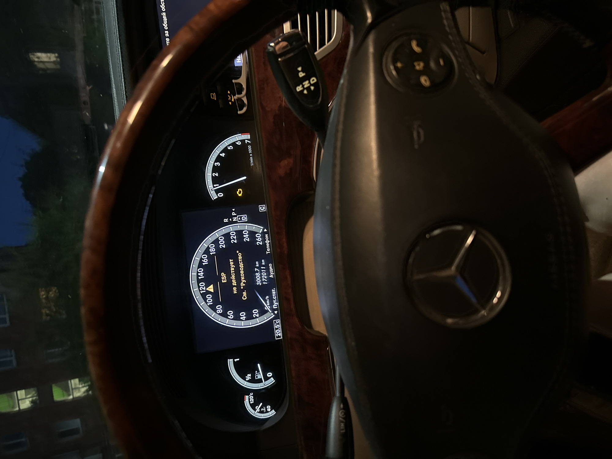 The image shows a close-up view of a car's dashboard and steering wheel. The dashboard displays various indicators, including speed (up to 260 km/h), engine RPM, temperature (120°C), and fuel level. An ESP warning light is illuminated, along with the text "не действует" and "См. "Руководство"". The car's mileage is 3008.7 km and the trip mileage is 172011 km. The current outdoor temperature is 20.5°C. The gear selector is visible, showing it is in "P" (Park) position. The Mercedes-Benz logo is prominent on the steering wheel. The background suggests an urban environment at night, with illuminated windows of buildings visible through the car's windshield. The image was taken in Blagoveshchensk, Russia.