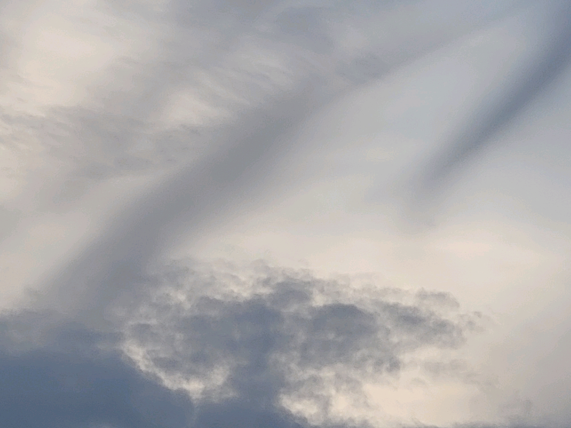 This image shows a cloudy sky above Ozolnieki, Latvia. The clouds are various shades of gray and white, with some appearing wispy and others more dense. The lighting suggests it may be overcast or nearing sunset. There are no people, animals, or man-made objects visible in the frame, only the natural elements of the sky.
