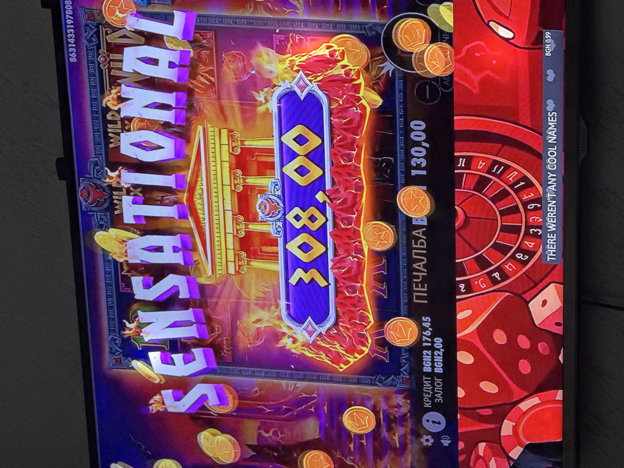 This is a photograph of a digital display showing a casino game. The game appears to be a slot machine with a Greek or Roman theme, indicated by the architectural elements and flaming effects. The word "SENSATIONAL" is displayed prominently. The numerical value "308.00" is shown, possibly representing a win amount. Other text includes "ПЕЧАЛБА B 130,00," likely indicating a payout of 130.00 in some currency. The phrase "THERE WEREN'T ANY COOL NAMES" is also visible. Currency indications include "BGN2 176,45" and "BGN2,00." The image also contains a roulette wheel and dice elements. There is no mention of Glojene, Bulgaria.