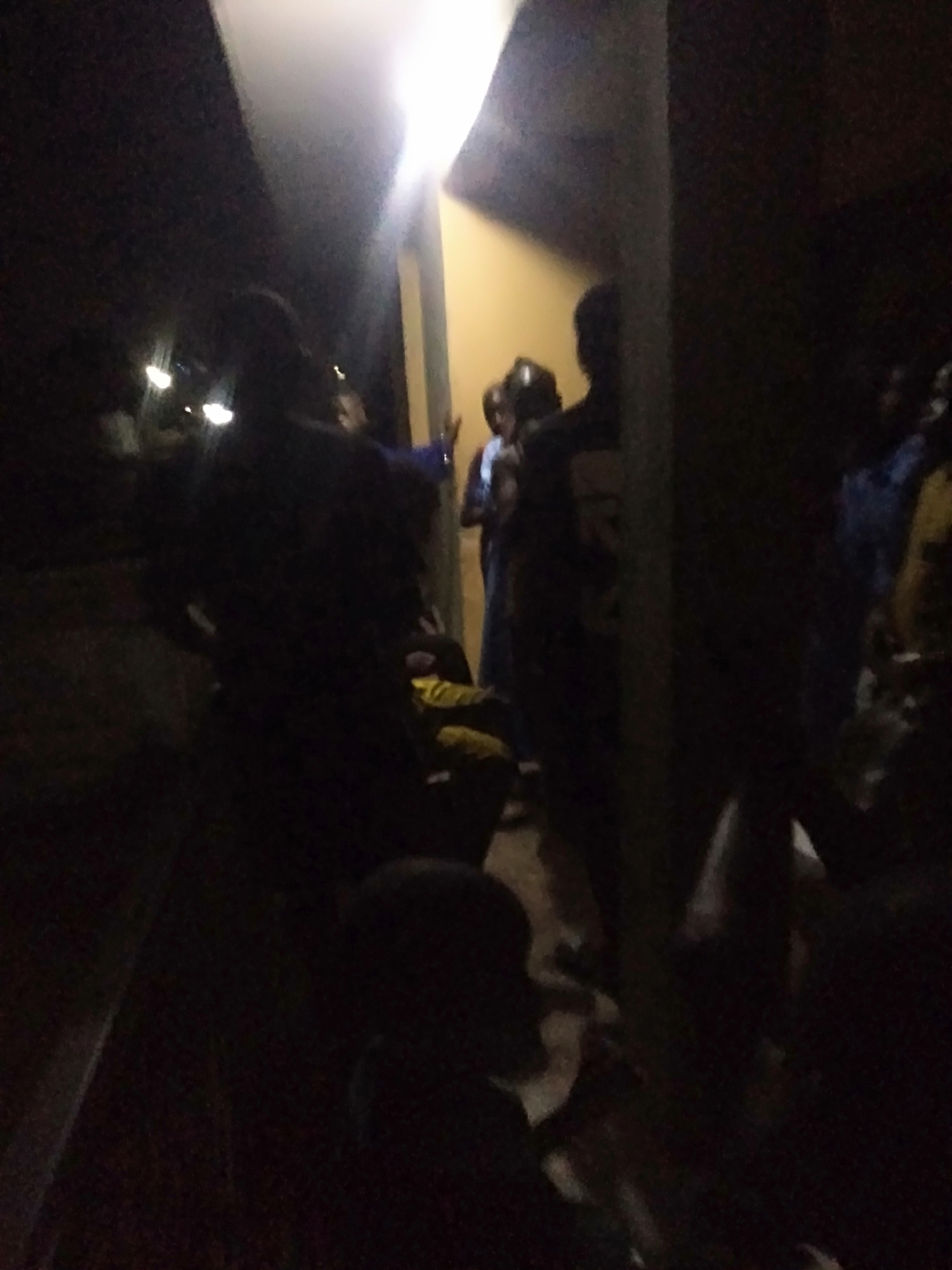 The image shows a group of people standing in front of a brightly lit doorway or opening at night. The location is possibly in Epe, Nigeria. Several people are visible, some more clearly than others due to the darkness and lighting conditions. They appear to be gathered near an entrance or doorway of a building. The overall environment is dark, with the bright doorway providing the main source of illumination.