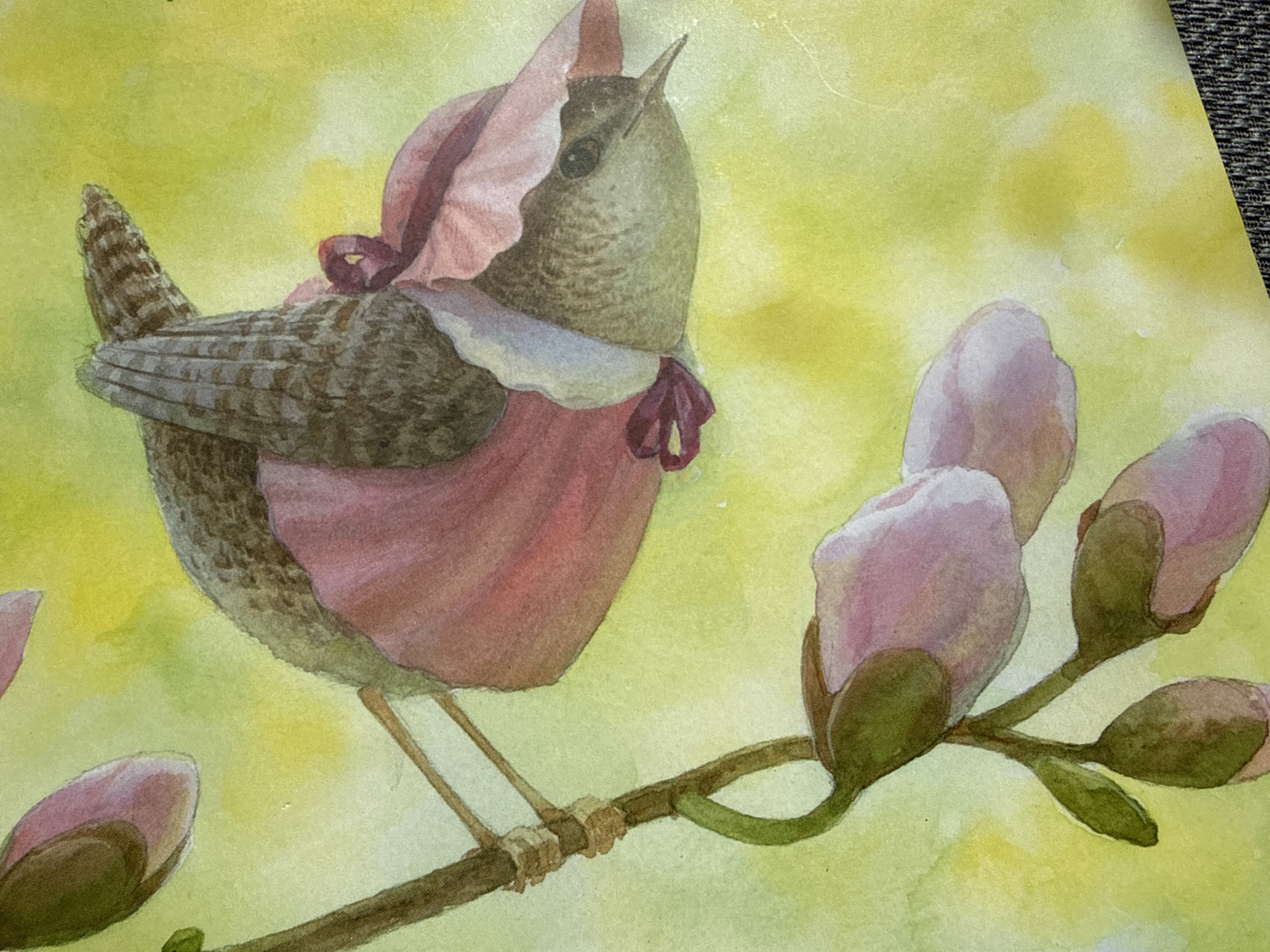 A watercolor painting depicts a small bird wearing a pink bonnet and dress, perched on a branch with pink flower buds. The bird's back is facing the viewer, with its head turned to the right, revealing its profile. The background is a wash of yellow and green watercolor. The painting is not located in Ridabu, Norway.