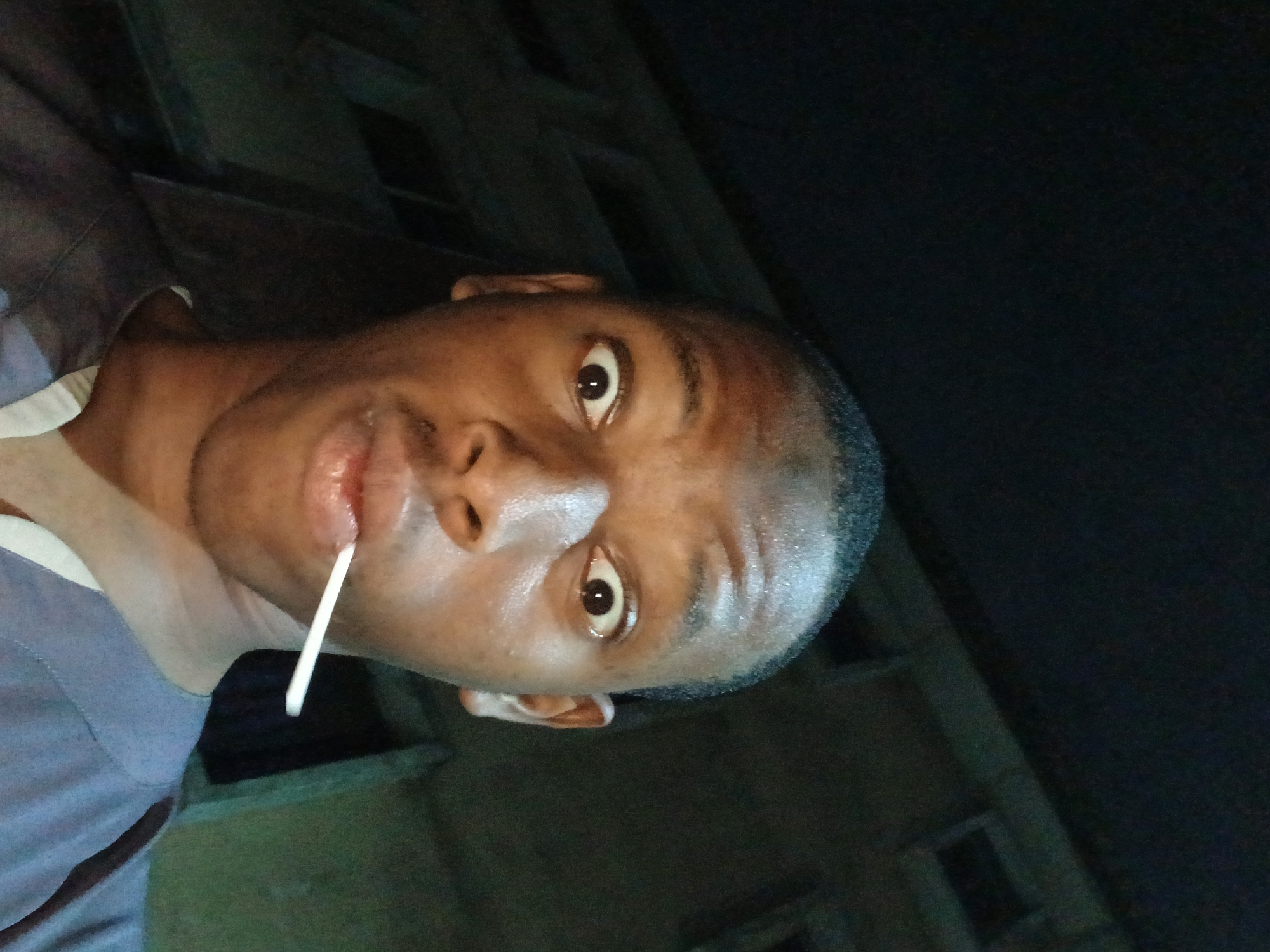 A man is holding a white lollipop in his mouth. The background suggests an urban environment at night. I am unable to identify the city or country.