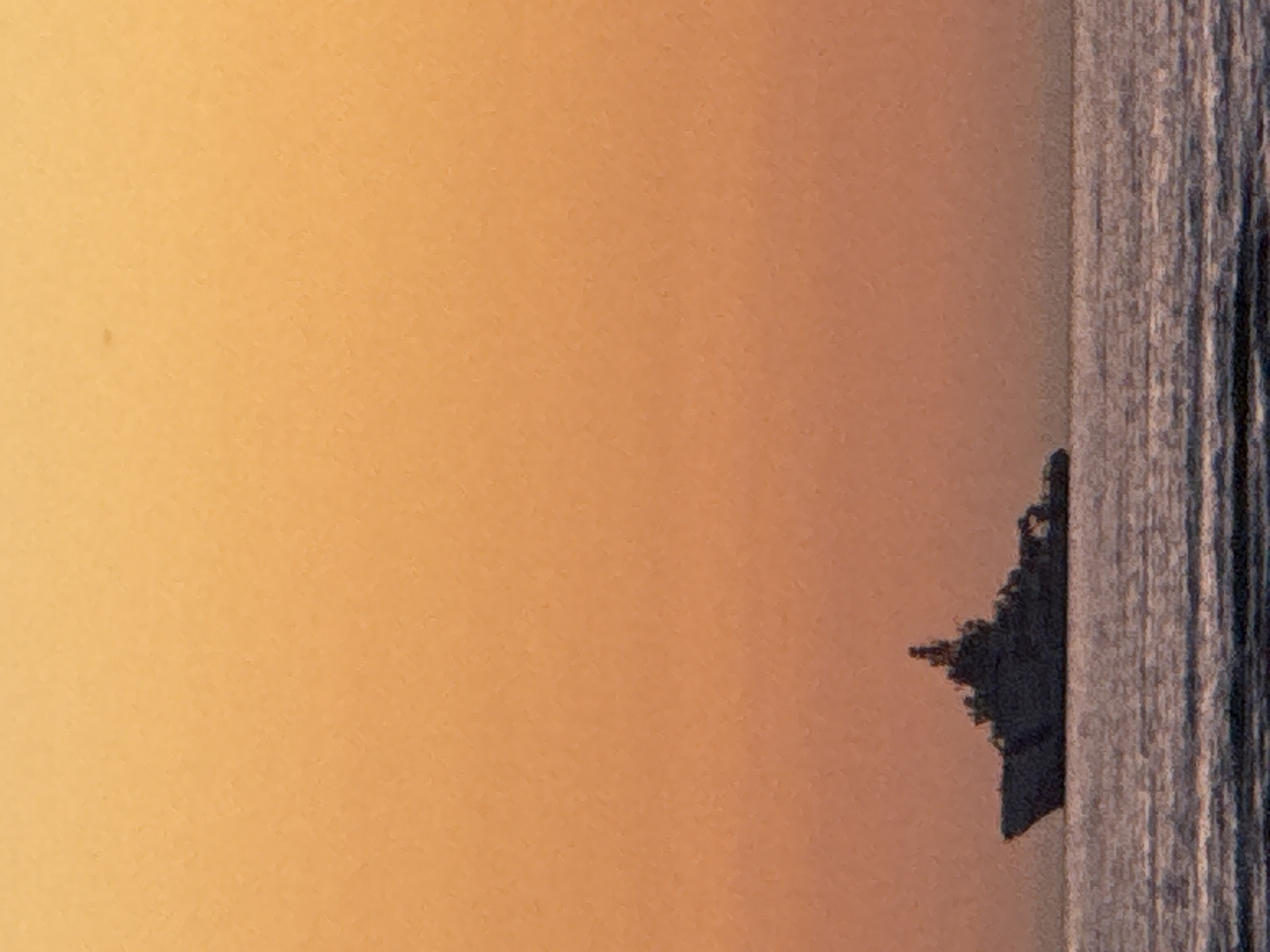 An image depicts a silhouette of a large warship sailing on the sea against a backdrop of an orange sky. The warship is dark and detailed, with visible structures and a prominent mast. The sea below is choppy with visible waves. The sky is a gradient of orange hues, suggesting either sunrise or sunset. There are no people visible in the image, nor any specific identifiable landmarks of Tallinn, Estonia.