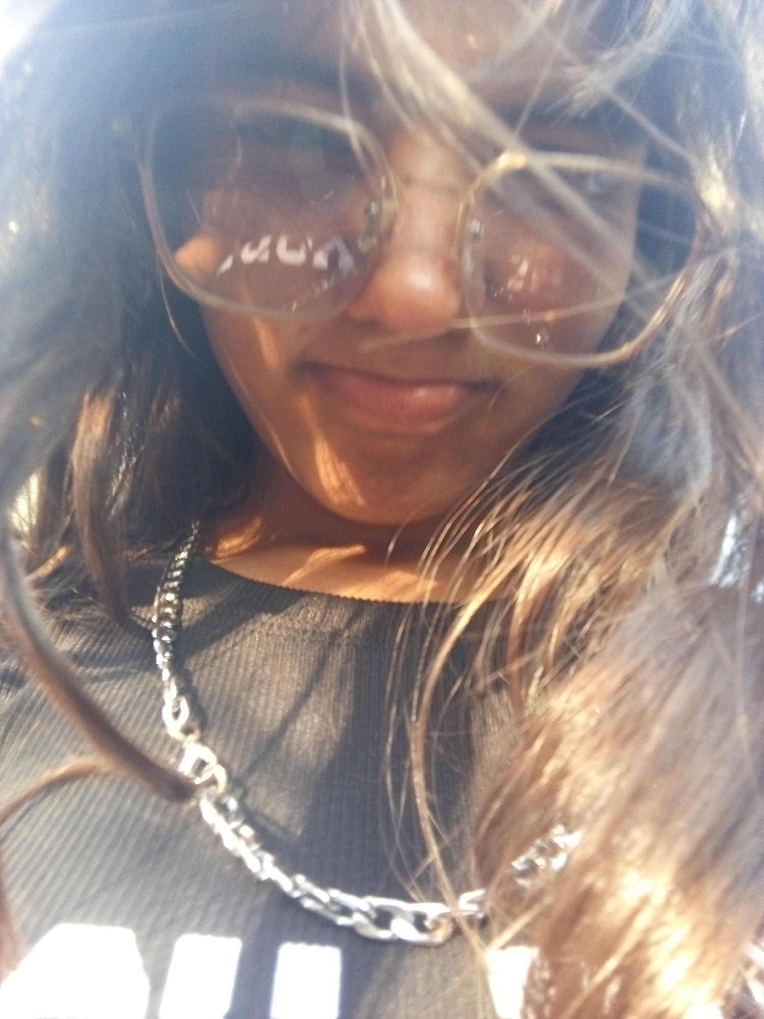 A selfie of a person with long, wavy brown hair wearing glasses and a silver chain. The person is wearing a dark top with a ribbed texture. The location of Juan Griego, Venezuela, is not discernible from the provided visual data.