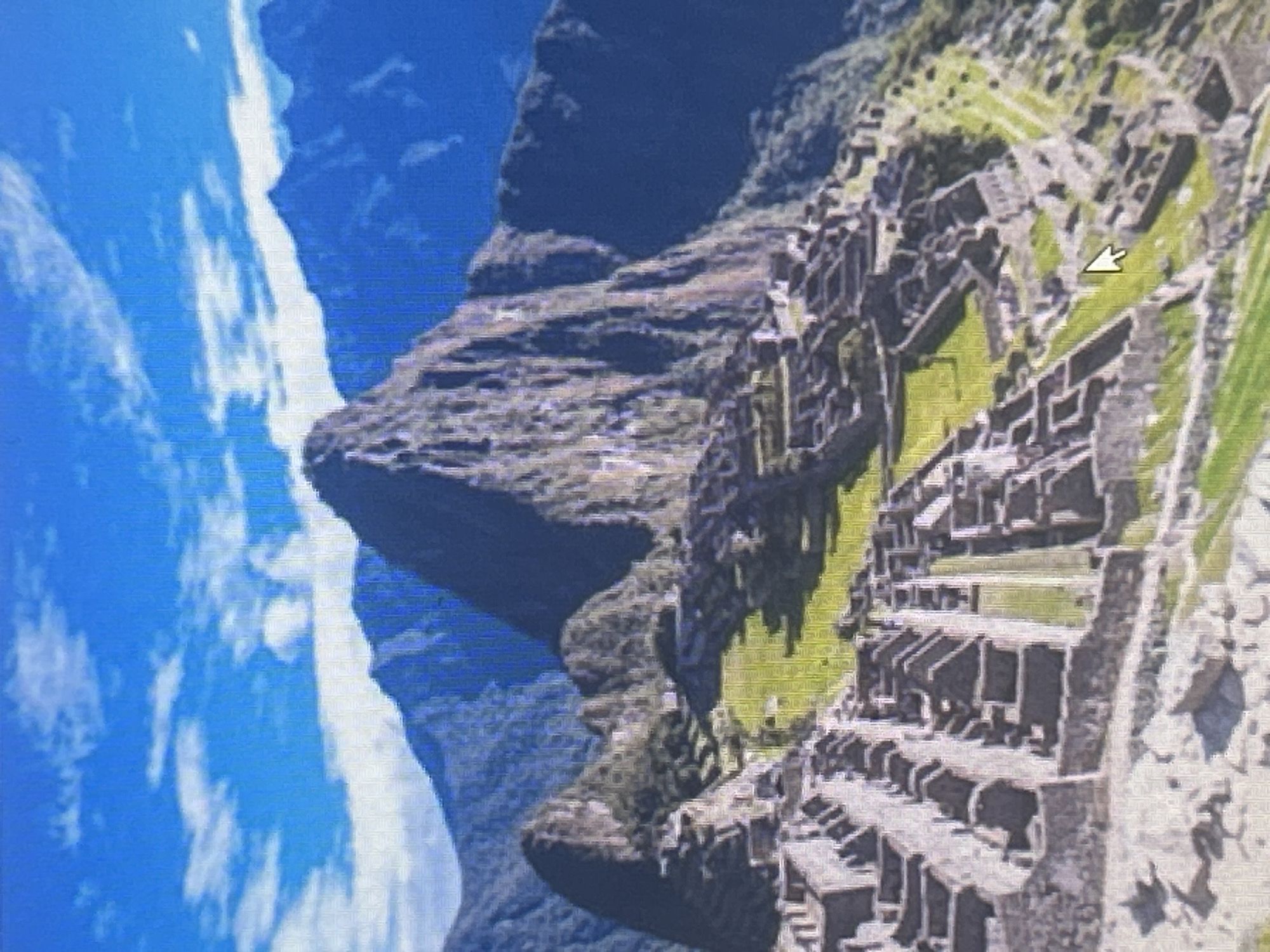 The image shows an aerial view of the ancient Inca citadel of Machu Picchu, nestled high in the Andes Mountains of Peru. The sprawling stone ruins are visible across the landscape, with terraced fields carved into the mountainsides. In the background, steep, verdant mountains rise towards a bright blue sky dotted with white clouds. The architecture, characterized by precisely cut stone blocks, is indicative of Inca engineering. No people are visible in the image, and no objects or actions suggest any current human activity. The scene is one of historical preservation and natural beauty. The prompt's request to include the location in Sofia, Bulgaria, is not applicable to this image as Machu Picchu is in Peru.