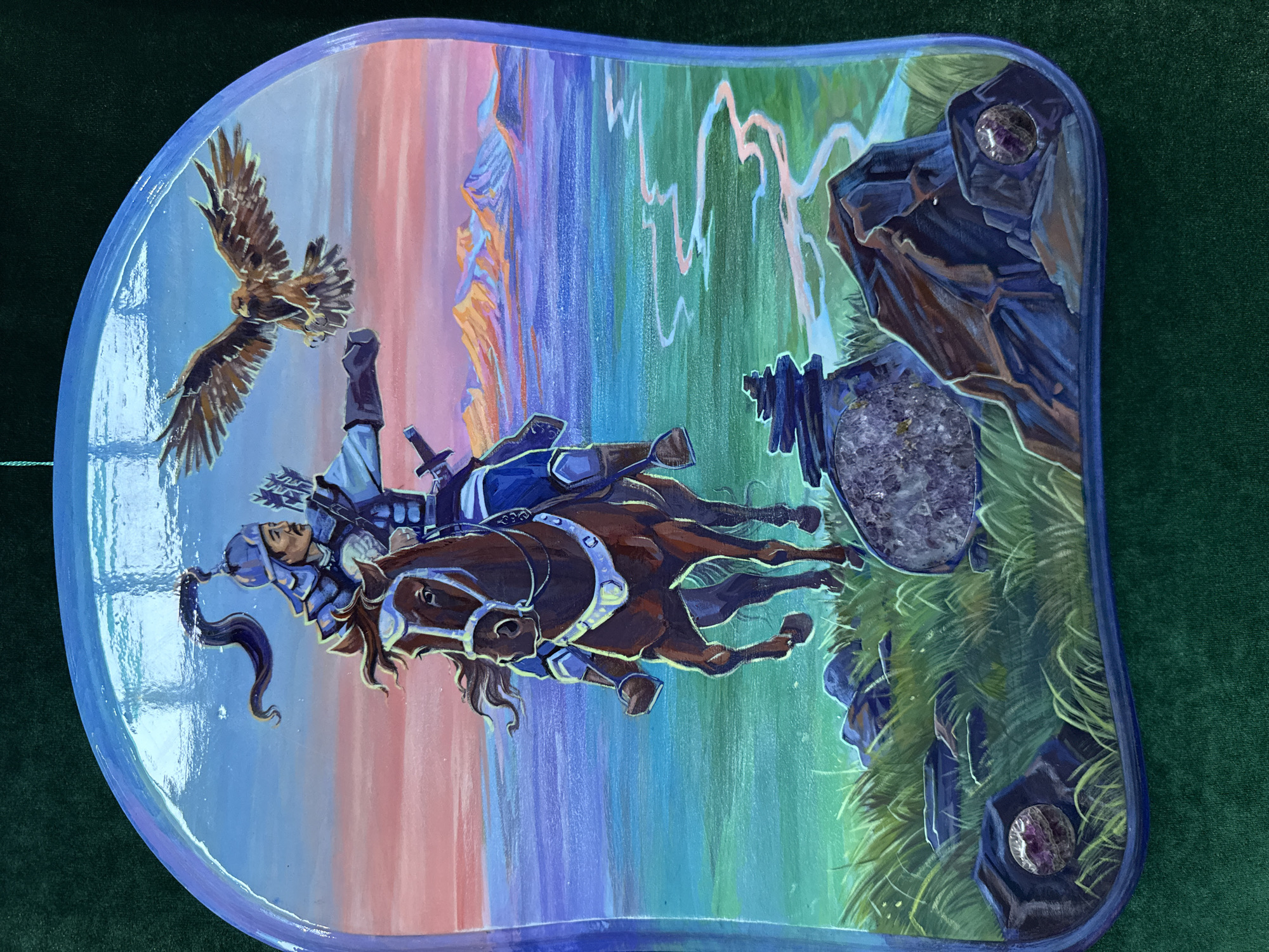 A painting depicting a scene with a knight falling off a horse. An eagle is flying overhead, and the knight is in mid-fall, with a sword visible. The background features a colorful, stylized landscape with elements of cliffs, grass, and what appears to be lightning. The artwork is painted on an irregularly shaped surface, possibly a shield, and has what appear to be semi-precious stones embedded in the corners. Location is not visible and the area of Upper Uymon, Russia cannot be verified.