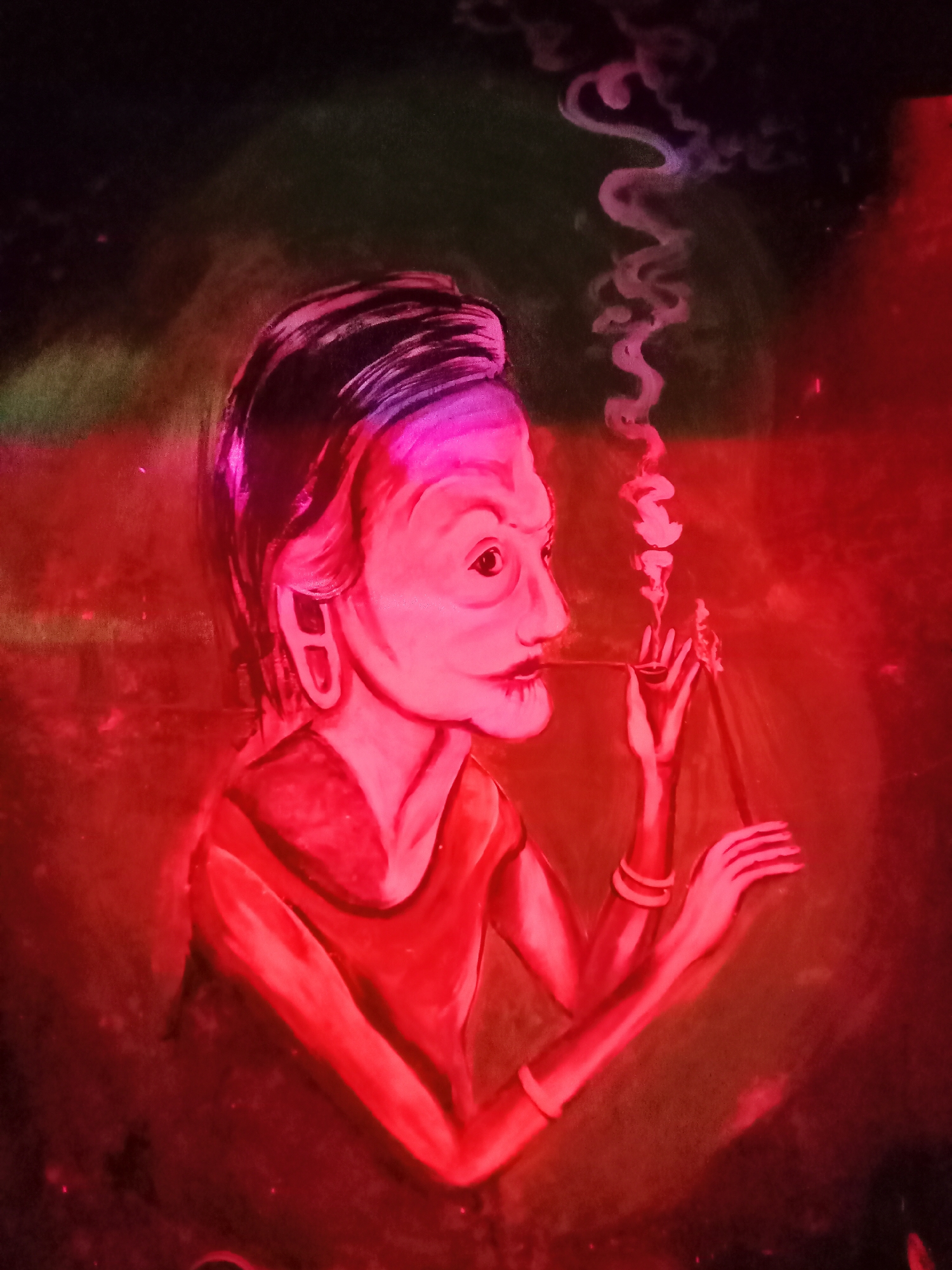 This striking image showcases a painting, possibly a mural, depicting an individual in profile, bathed in a dominant red light. The subject is an older person, likely a woman, with distinct facial features including a prominent nose, high cheekbones, and a focused gaze. Her dark hair is pulled back, revealing a large, D-shaped earring on her visible ear.
She is engaged in the act of smoking, holding a long, slender pipe with both hands towards her mouth. Wisps of white smoke elegantly ascend from the pipe, forming sinuous patterns against the dark background. The intense red illumination casts a dramatic glow, transforming skin tones into vibrant pink and crimson hues, and saturating the surrounding environment with rich reds. The background is a blend of dark tones with subtle hints of green, contributing to a mysterious and atmospheric setting.
The subject's expression appears calm and contemplative, suggesting a moment of quiet reflection or tradition. The strong, almost monochromatic lighting creates a surreal and stylized aesthetic, giving the artwork a powerful visual presence. No specific time of day or weather conditions are discernible, and while the image itself lacks explicit location cues, the provided context places it in Nha Trang, Vietnam. No text is visible within the image.