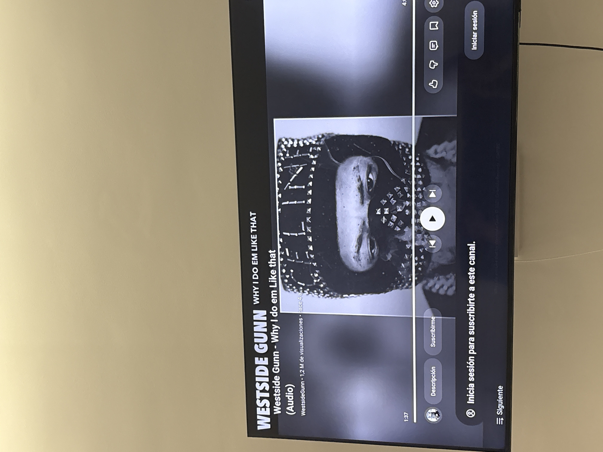 The image shows a television screen displaying a YouTube video of Westside Gunn's song "Why I Do Em Like That." The video is in audio format and has 1.2 million views. The viewer has the option to subscribe to the channel or sign in. The video is at the 1:37 mark. The screen displays options for description, subscription, and next video. The TV is mounted on a light beige wall. The image does not provide information about the location in Barcelona, Spain.