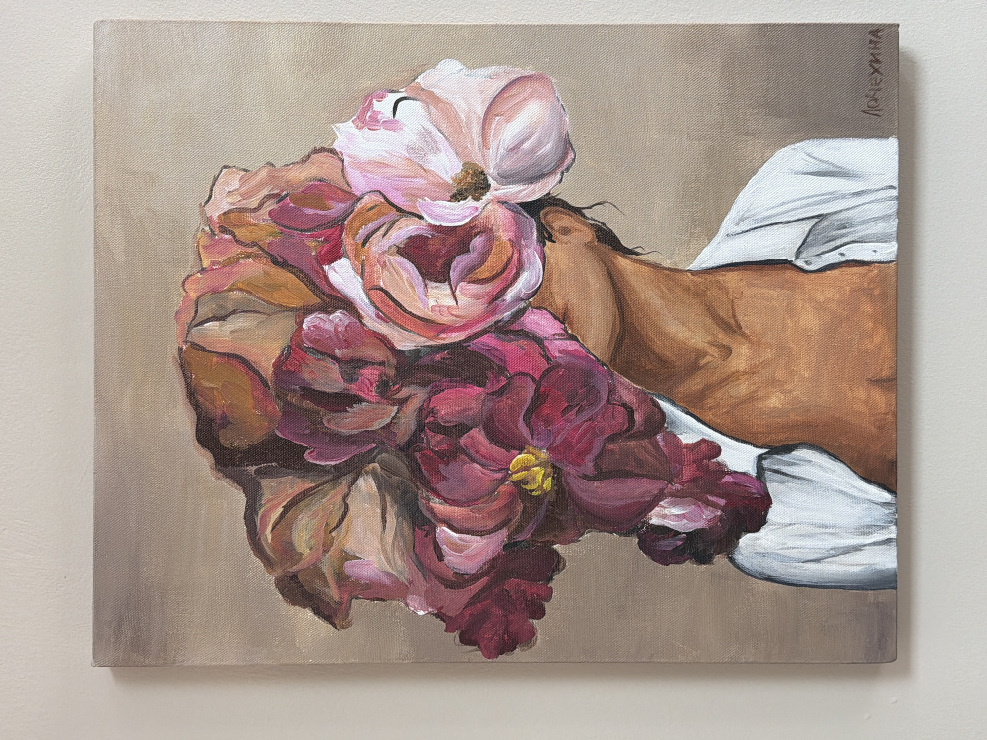 The image is a close-up of a painting on canvas. The painting depicts a person's face lying among flowers. The skin tone of the person is brown, contrasting with a white shirt or sheet near the edge of the canvas. A bouquet of flowers in shades of pink, burgundy, and cream dominates the left side of the painting. The background is a muted beige or tan. The signature “Логухина” is written vertically on the right side of the canvas. The painting style is somewhat impressionistic with visible brushstrokes. The image is mounted on a plain off-white wall. There is no indication this image is connected to Krasnoyarsk, Russia.