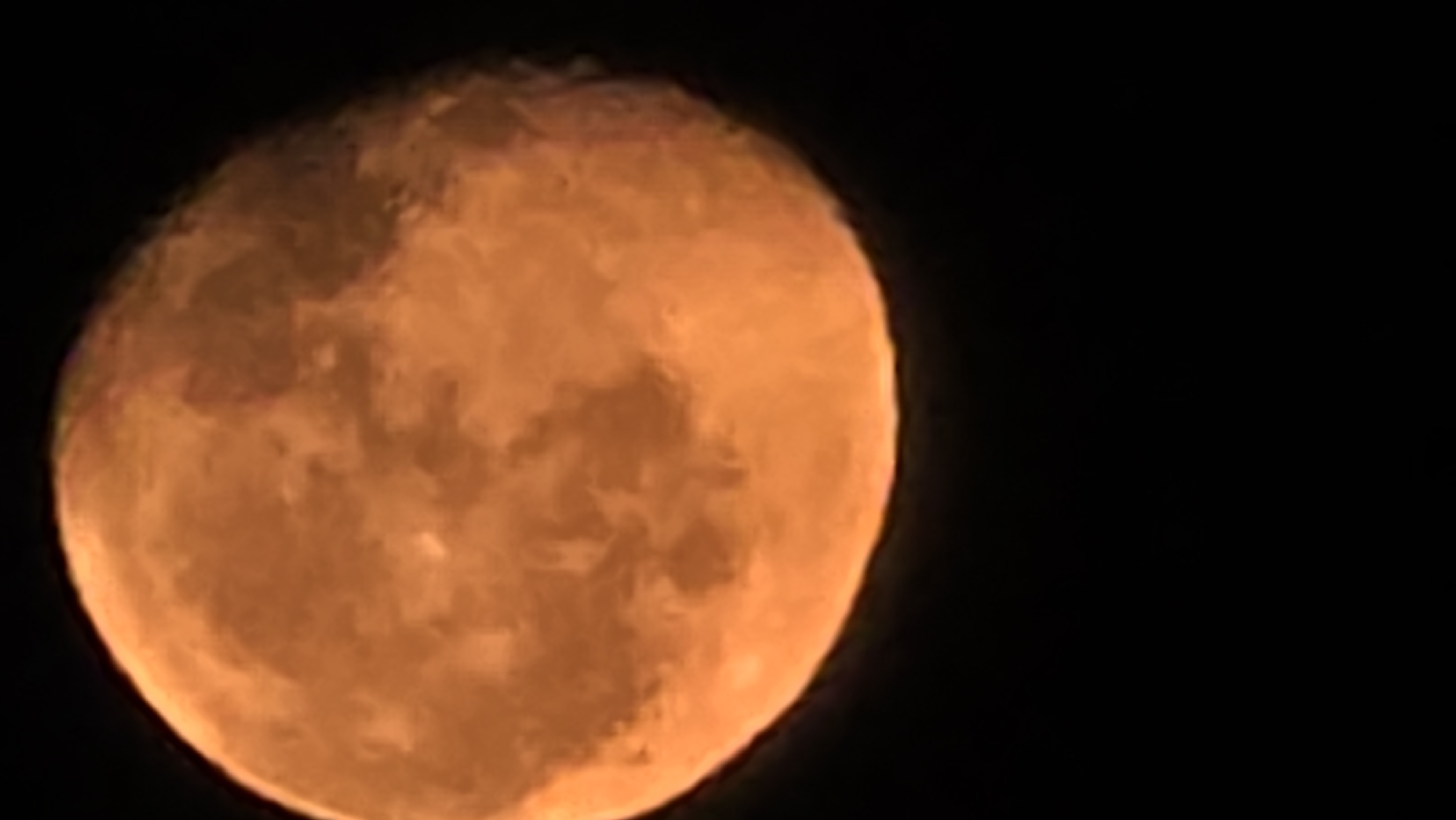 The image shows a close-up of the moon, illuminated with an orange hue and displaying surface details. The background is black, indicating a night sky. The location in the city of Krasnodar, Russia, cannot be determined from the image content alone.