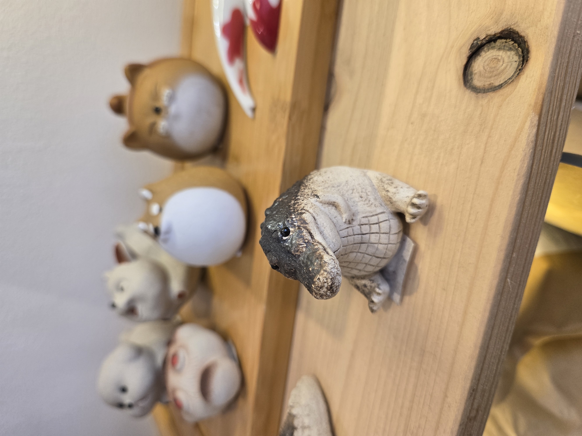 A wooden wall is adorned with a collection of small, whimsical figurines. The figurines include animal shapes like bears, a pig, and a reptile that appears to be an alligator or crocodile. The location in Budva, Montenegro is not discernible from the image.