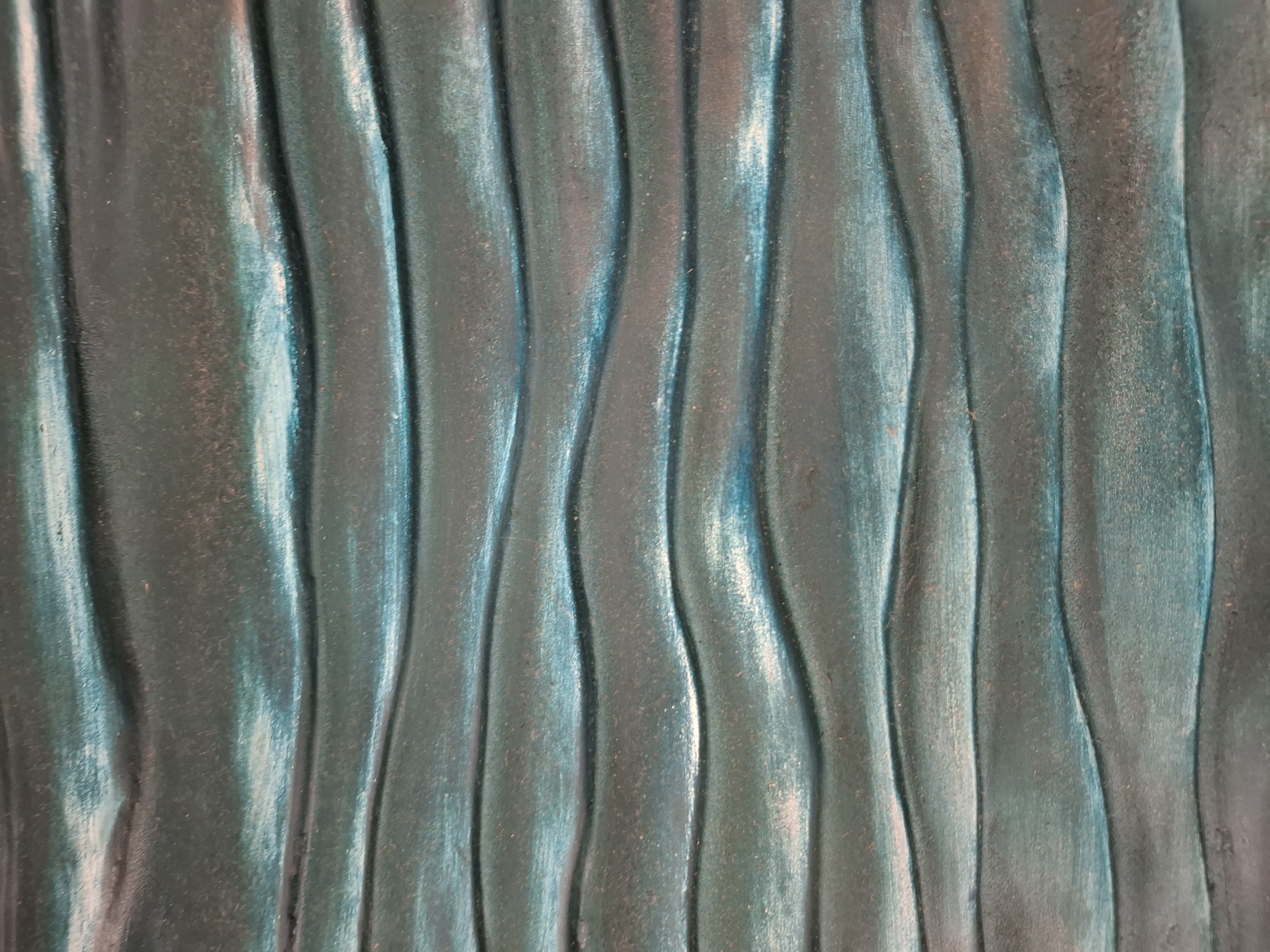 The image is a close-up, abstract view of a textured surface with horizontal, wavy ridges. The color is a blend of deep teal, muted green, and hints of metallic copper or bronze, giving it a weathered or patinated appearance. The lighting creates highlights and shadows that accentuate the undulating pattern of the surface, suggesting a material like distressed metal, carved wood, or a textured ceramic tile. The surface appears to be a flat panel, with the waves running from left to right across the frame. There are no discernible people, animals, or specific objects that can identify the location as Phu Thuy Ward, Vietnam. The image is purely a textural study of a decorative or architectural element.