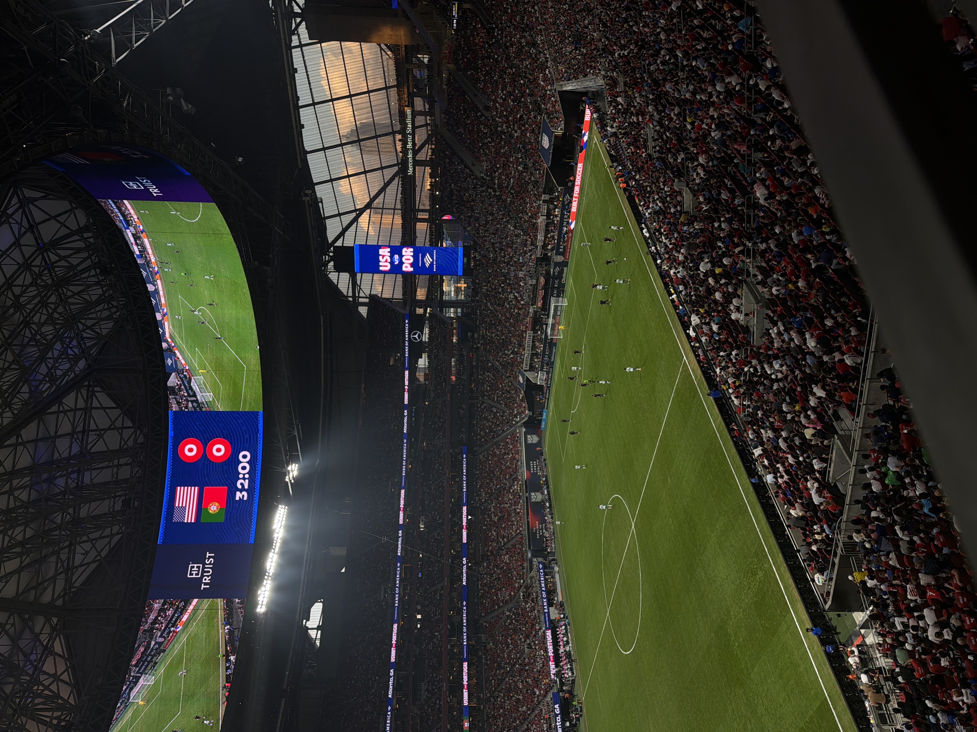 The image captures a soccer game between the USMNT and Portugal at the Mercedes-Benz Stadium in Atlanta, GA. The stadium is filled with spectators. The score shows a 0-0 tie at the 32:00 mark. A large screen displays the game action. Sponsorships such as Truist and Bank of America are visible.