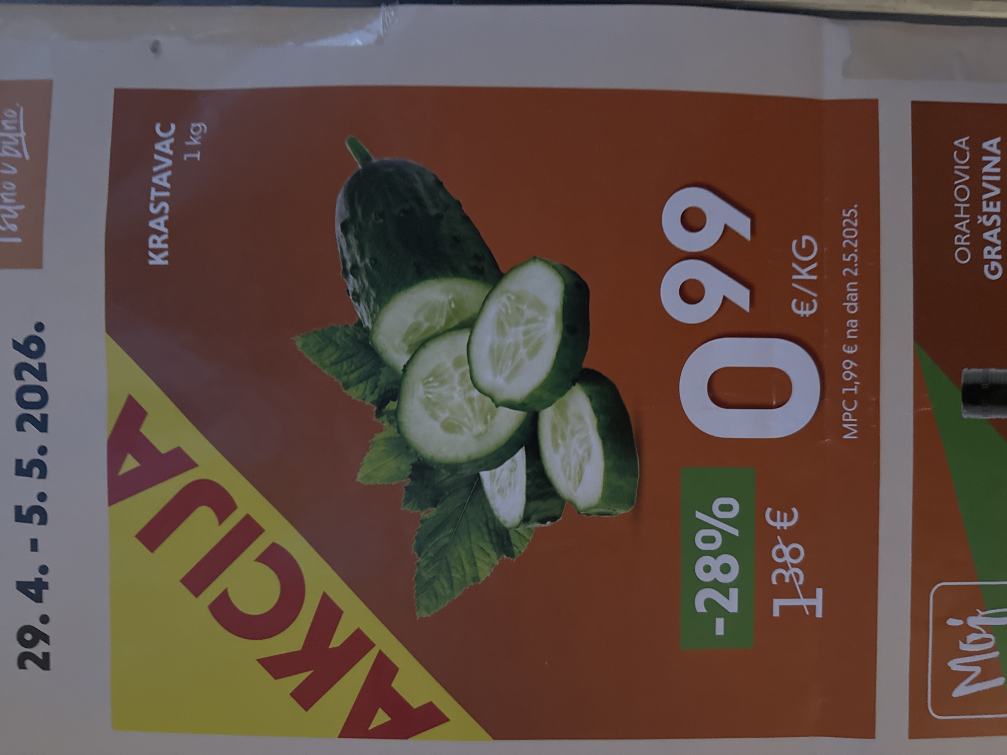Here is a detailed description of the image:
**Overview:** The image is a cropped section of an advertisement, likely from a flyer or magazine, showcasing a special offer on cucumbers.
**Details:**
* **Text:** The flyer includes the following text:
* Dates: "29.4. - 5.5.2026"
* "AKCIJA" (Croatian for "SALE")
* Product: "KRASTAVAC" (Croatian for "CUCUMBER") "1 kg"
* Price: "099 €/KG"
* Discount: "-28%"
* Original Price: "138 €"
* "MPC 1,99 € na dan 2.5.2025." (refers to the previous price on May 2, 2025)
* Another product with text reading: "ORAHOVICA GRAŠEVINA"
* **Imagery:** A picture of a cucumber along with sliced sections of cucumber.
* **Brand:** There is text with "Moj" (Croatian for "Mine").
* **Color Scheme:** The flyer utilizes a color scheme of reds, yellows, greens, and whites.
**Possible Location:** Given the language (Croatian) and the product names, the advertisement likely originates from Croatia, possibly the City of Zagreb.