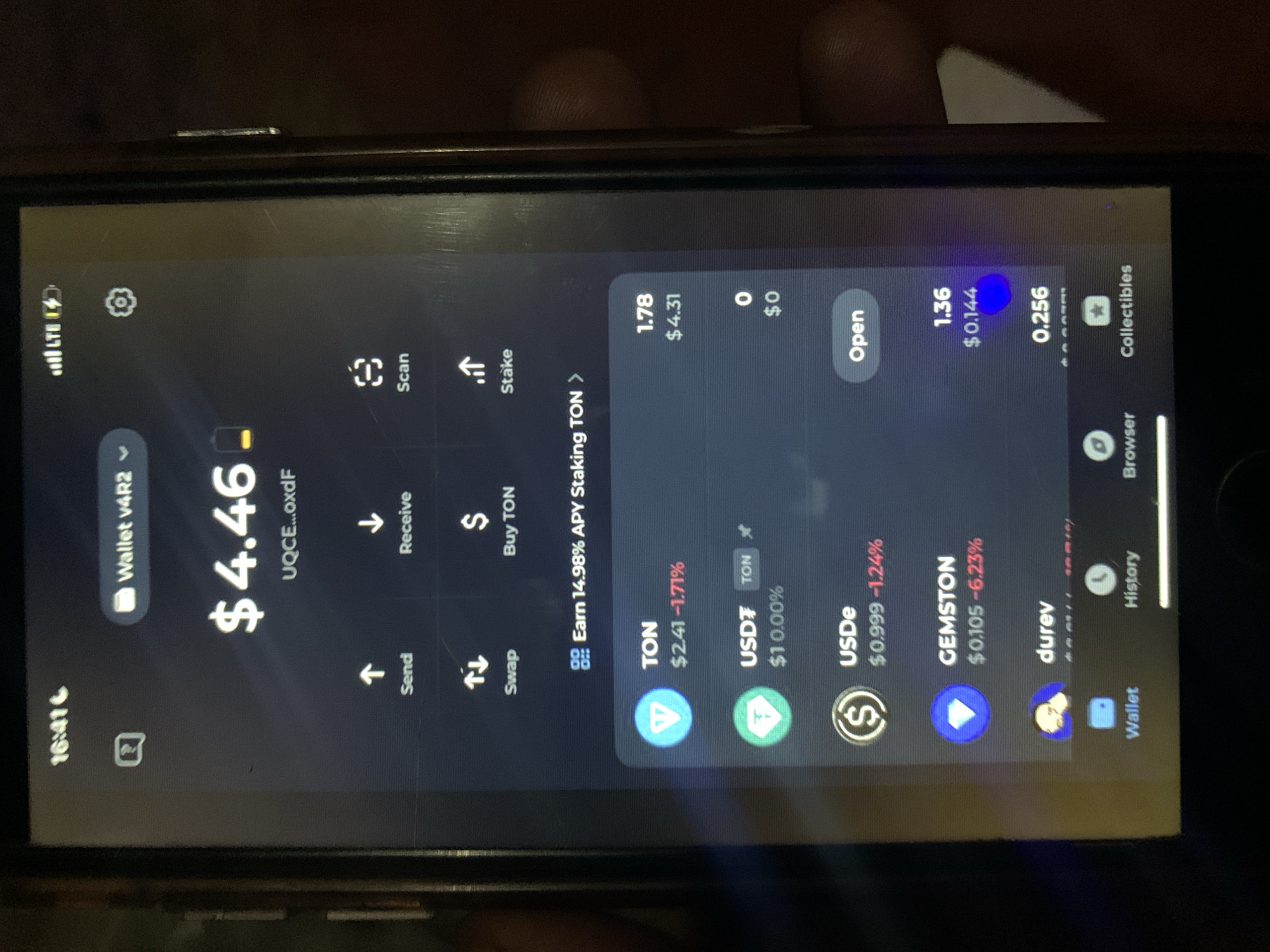 The image depicts a smartphone screen displaying a cryptocurrency wallet interface. The wallet balance is $4.46. The user can send, receive, swap, and buy TON. The wallet also shows an option to stake TON with a 14.98% APY. Listed cryptocurrency balances include 1.78 TON ($4.31), 0 USDe ($0), 1.36 GEMSTON ($0.144), and 0.256 durev. The phone's status bar shows the time as 16:41. The environment is not depicted.