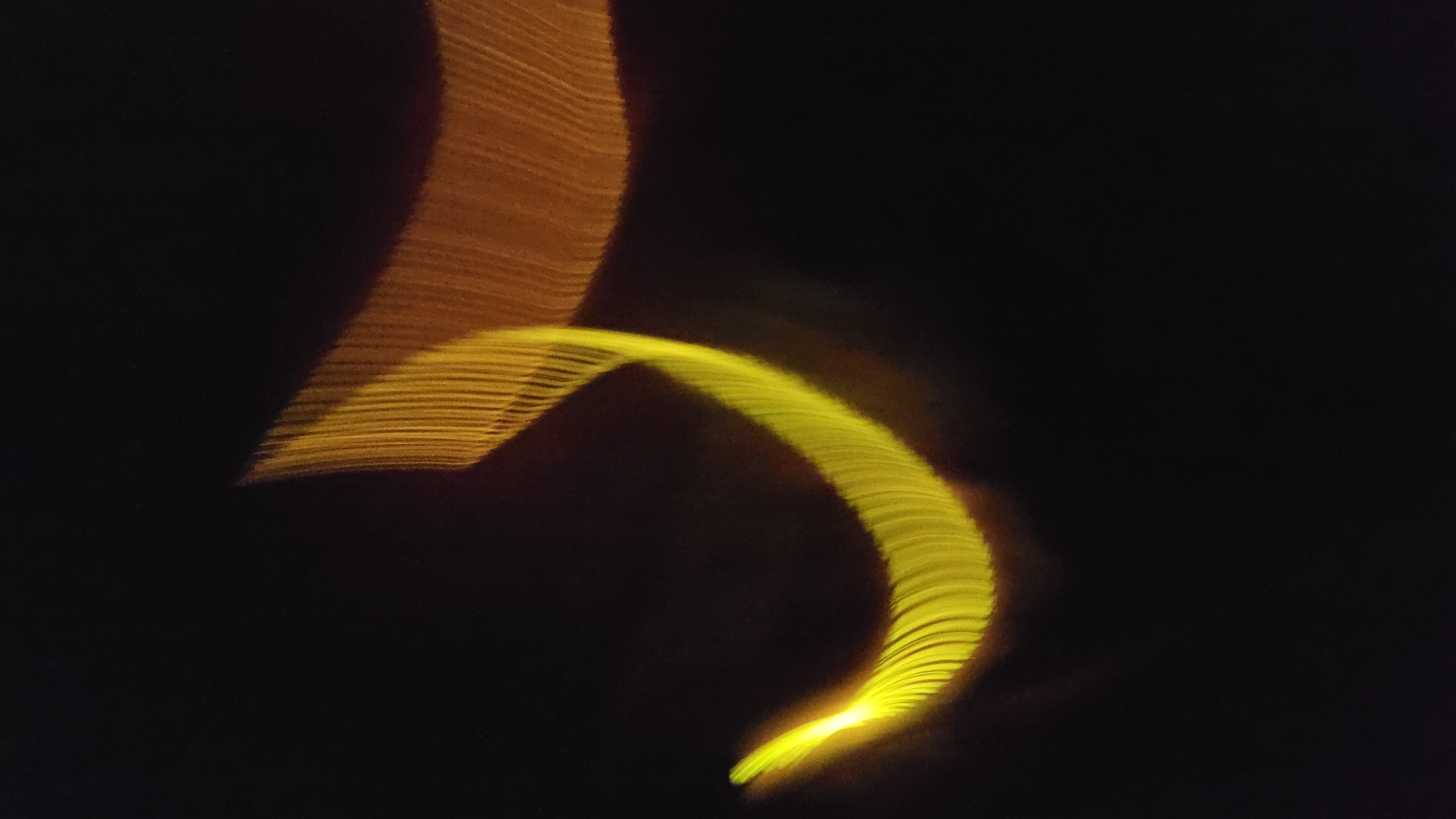 A long exposure photograph shows blurred yellow and orange light streaks against a black background. The streaks are curved and have a textured appearance. Location: Cam Đức, Vietnam.