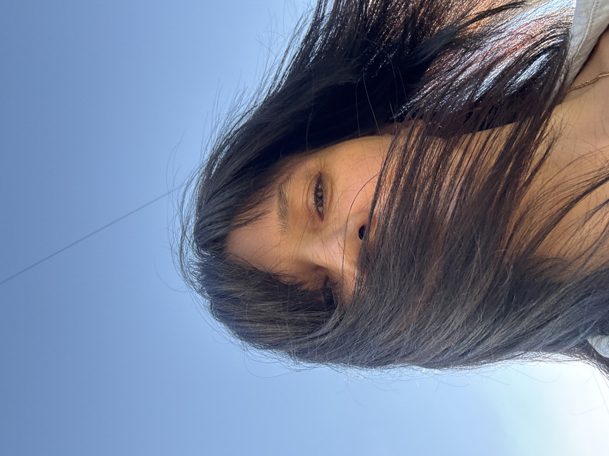 A low-angle, upside-down view shows a person with long, dark hair obscuring most of their face. One eye is visible. The background is a clear blue sky. The location of the photo cannot be determined to be Chaikovsky, Russia from the image alone.