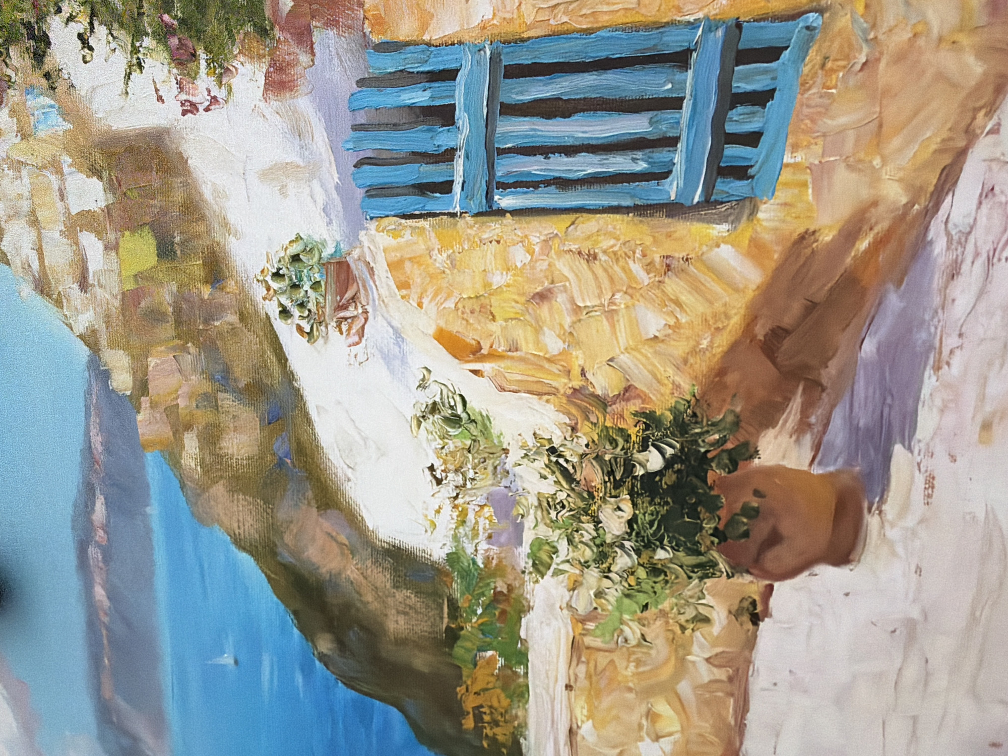 This is a close-up, oil painting depicting a sun-drenched Mediterranean coastal scene. The foreground is dominated by a textured, stucco wall painted in warm, earthy tones of yellow and orange, with a white-washed section on the left. A vibrant blue shuttered window is a prominent feature, set against the textured wall. To the left of the window, a terracotta pot holds lush green foliage, casting a shadow on the white ground. Further down and to the left, another, larger terracotta pot contains a more elaborate green plant. The background reveals a steep, rocky hillside leading down to a bright blue sea. A small white sailboat is visible on the water, and distant hills are rendered in soft blues and purples. The painting style is impressionistic, with visible brushstrokes adding to the texture and light effects. There is no indication of the city of Kyiv, Ukraine, in this image.