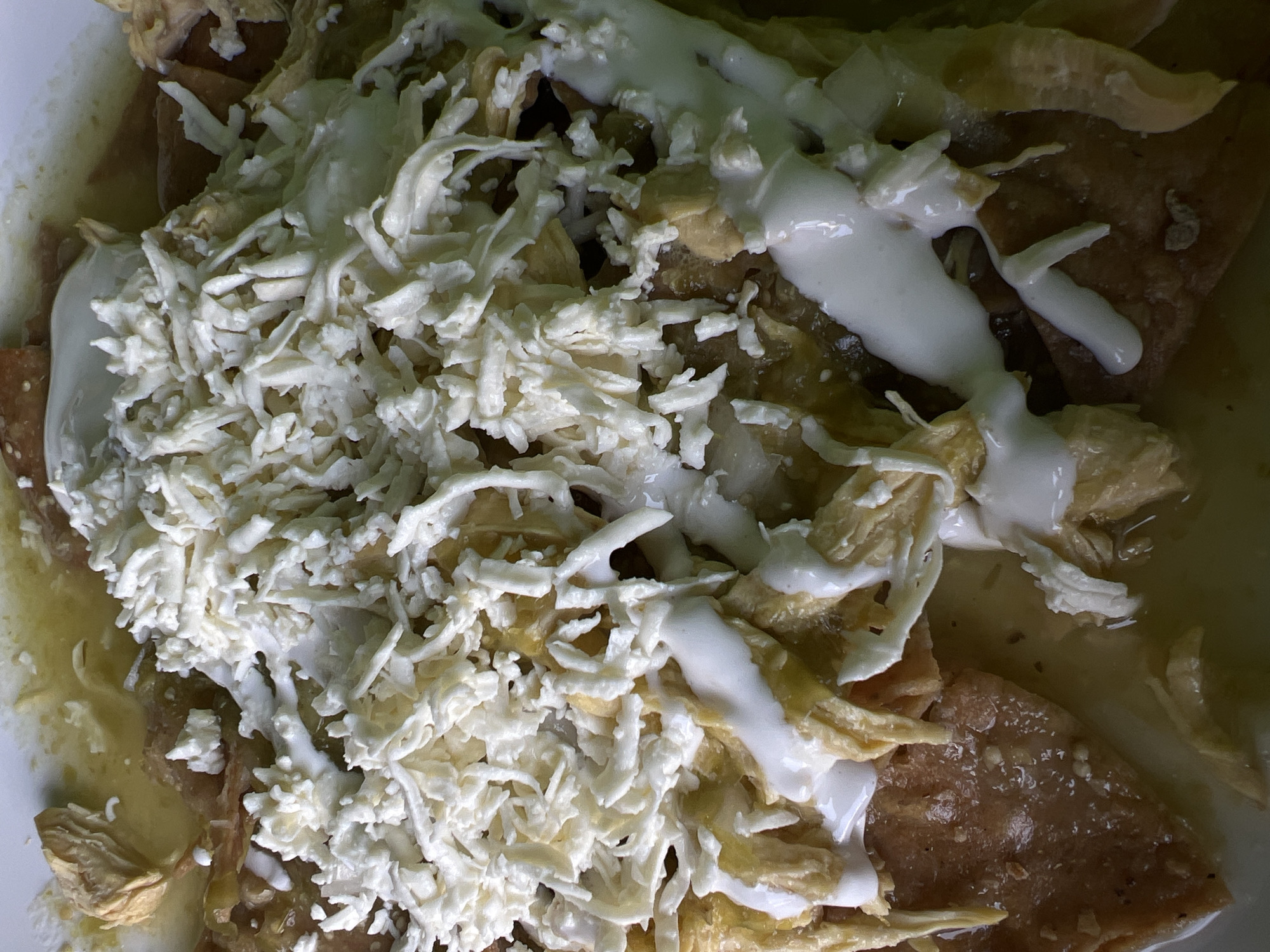 A close-up shot shows a plate of enchiladas, a traditional Mexican dish. The enchiladas are topped with shredded cheese and a drizzle of white cream. The dish is likely located in Mexico City, Mexico, given its cultural origin. The focus is solely on the food, with no people or other objects visible in the frame. The environment is limited to the plate and its contents.