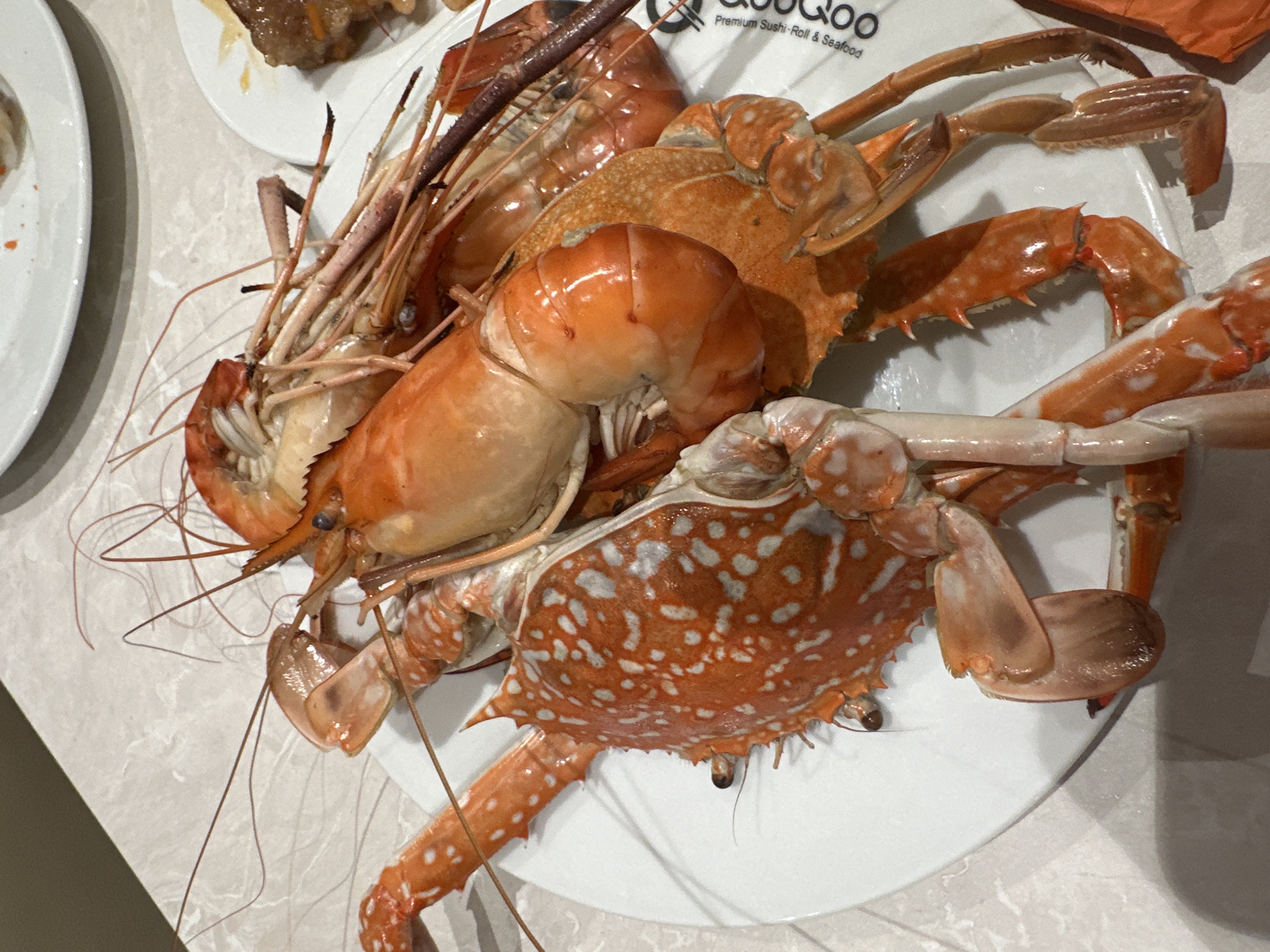 A top-down, medium shot shows a white plate filled with cooked seafood, including several large shrimp and two crabs. The seafood appears to be served on a round, white plate, which is sitting on a marbled surface. Some of the shrimp are stacked together, while the crabs are positioned around them. The location might be in Nha Trang Ward, Vietnam.