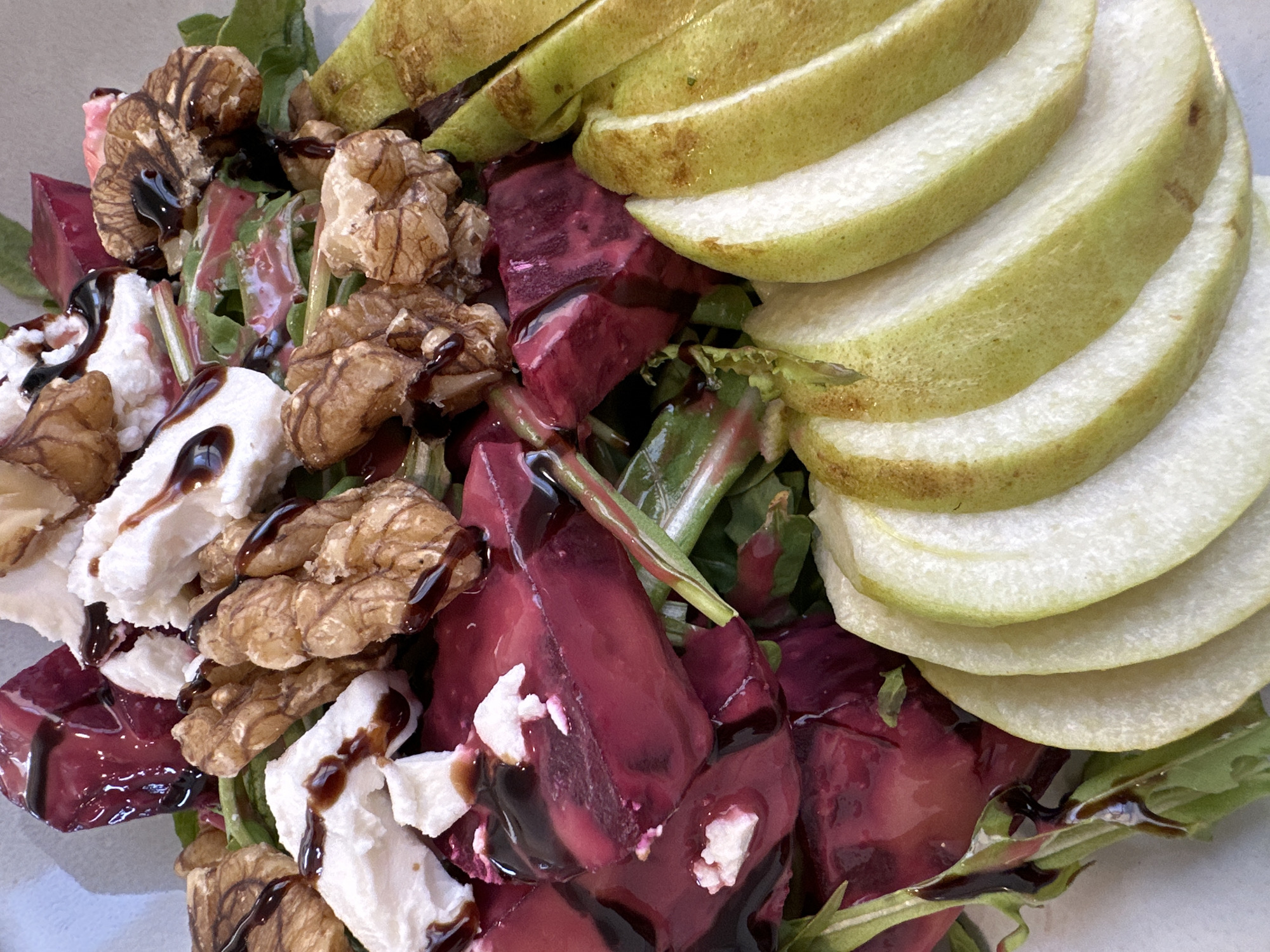 A close-up shot captures a vibrant salad with sliced pears, beets, goat cheese, and walnuts, drizzled with a dark balsamic glaze. The salad is arranged on a light-colored surface. The image does not contain any information or context related to a specific location in ตำบลเกาะพะงัน, Thailand.