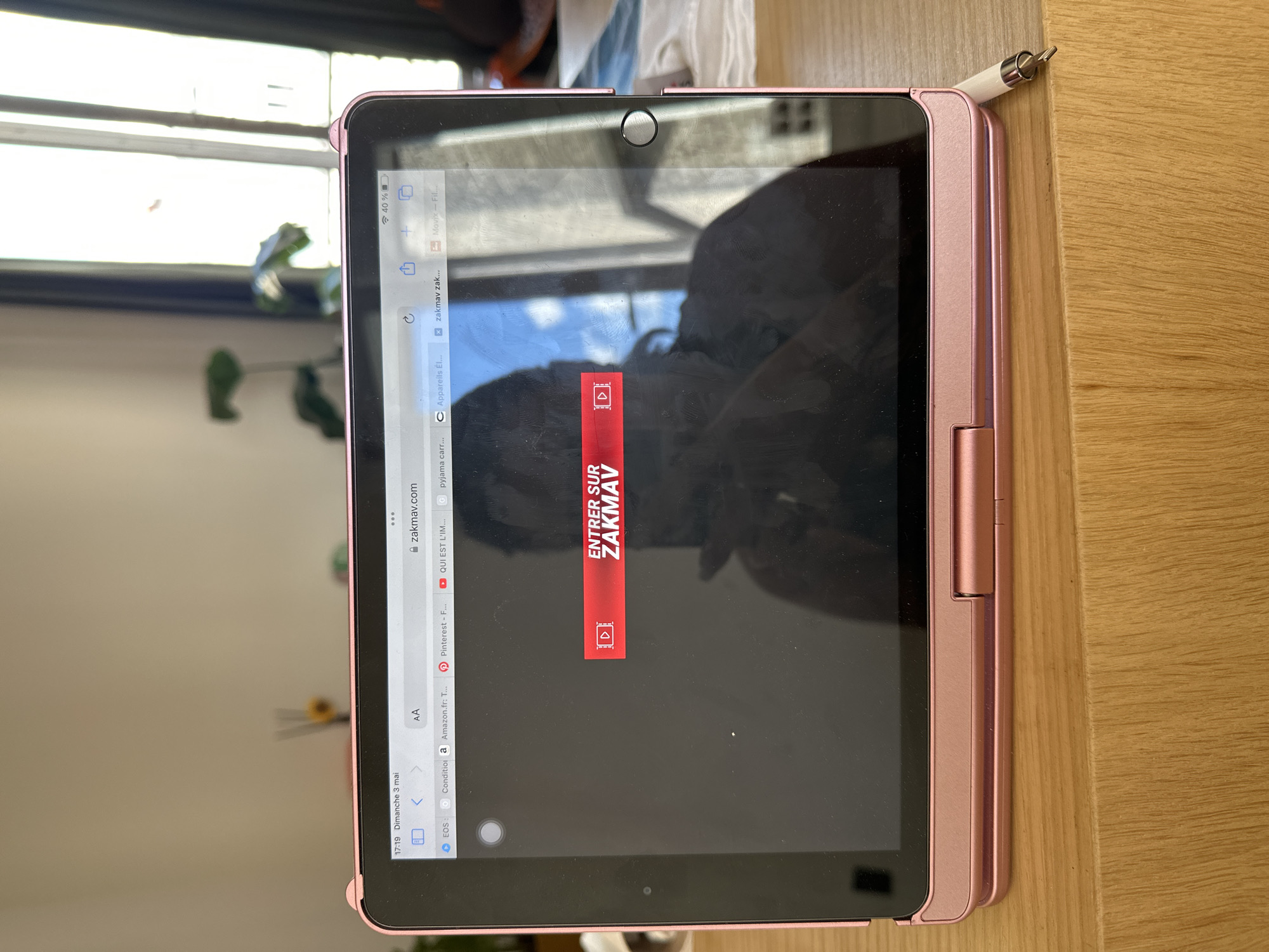 A pink iPad is on a wooden surface. The screen displays a web browser window navigated to the website "zakmav.com". An overlay in the center of the screen reads "ENTRER SUR ZAKMAV". The iPad is next to a white stylus. A window with a glimpse of the outdoors is partially visible in the background. The location is Saint-Ouen-sur-Seine, France.