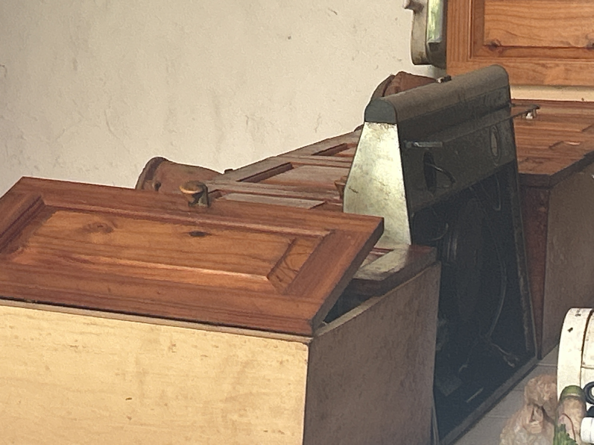 The image shows a close-up view of a kitchen area, likely within a residential setting. The dominant elements are wooden cabinets, a metallic range hood, and a textured ceiling. The cabinets, made of what appears to be a reddish-brown wood, are of a traditional design with visible wood grain and decorative molding. One cabinet door is slightly ajar, revealing a glimpse of the interior. The metallic range hood, positioned beneath the cabinets, is dark and somewhat grimy, suggesting regular use. Above the cabinets and hood, a light-colored, textured ceiling is visible. The overall lighting suggests an indoor environment, possibly with natural light supplemented by artificial sources, although no direct light sources are clearly identifiable. There are no people or discernible actions occurring in the image. The scene is static and focused on the architectural and functional components of a kitchen. The location is identified as being in Santa Ana, Venezuela.