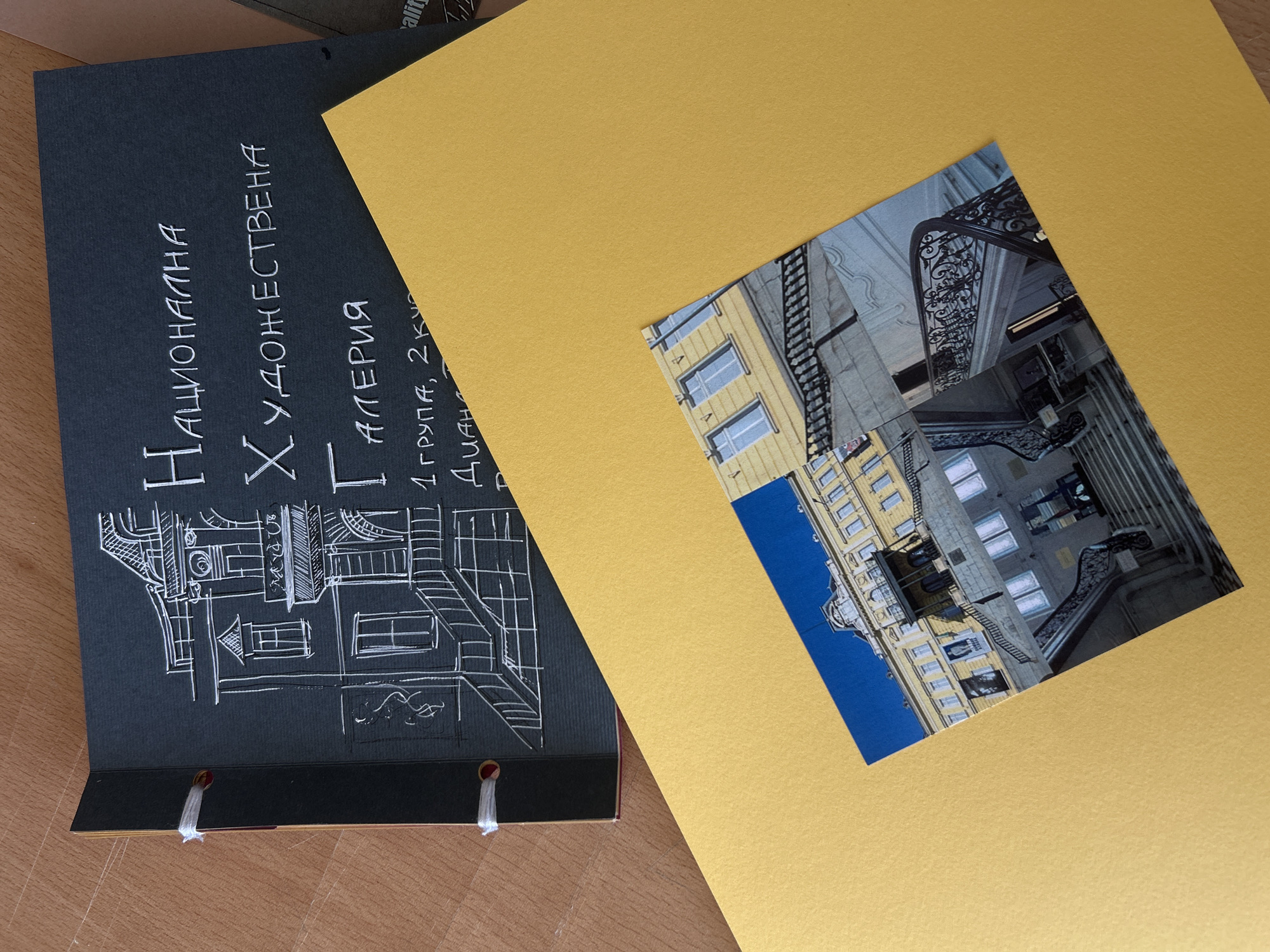 The image shows a dark-colored scrapbook with white handwriting and drawings, partially open and resting on a yellow sheet of paper. The scrapbook's cover features a sketched architectural design, likely a building with windows and a staircase. Handwritten text in Bulgarian is visible, including "Национална Художествена Галерия" (National Art Gallery), "1 група, 2 ку" (Group 1, 2nd year/grade), and "Диана" (Diana). A photograph is placed on the yellow paper, depicting a grand building with a prominent staircase and windows. This building is the National Art Gallery, located in Sofia, Bulgaria. The scene appears to be set indoors or on a desk, with the scrapbook and photograph being the central subjects.