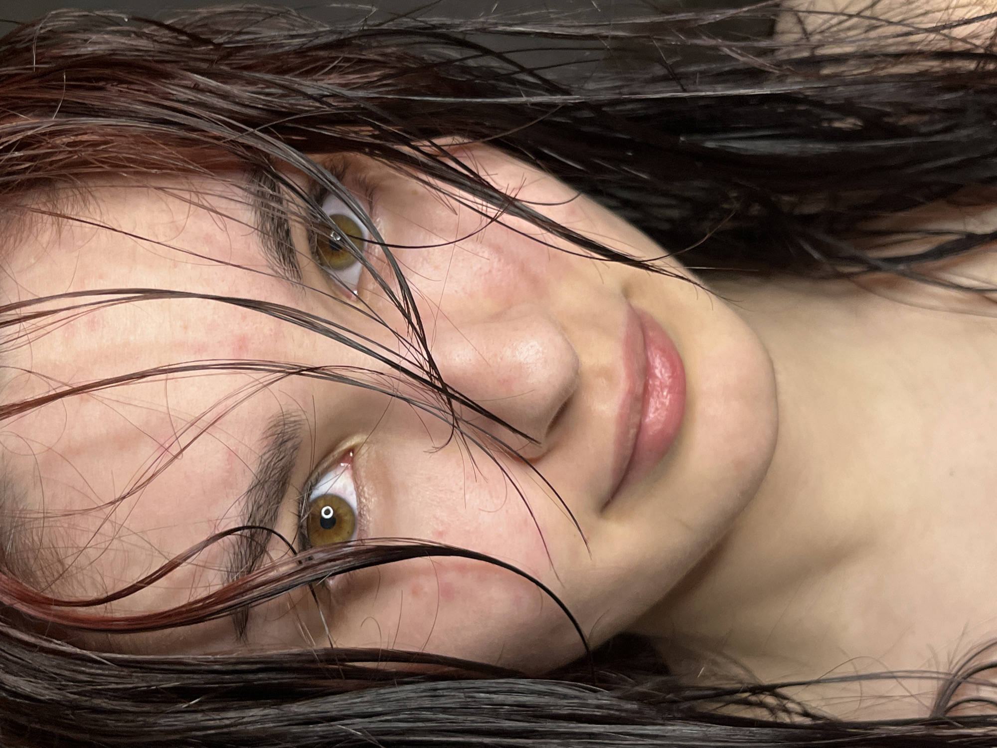 Close-up, angled portrait of a young woman with wet, dark brown hair partially obscuring her face. She has light skin, brown eyes, and slightly parted pink lips. Her gaze is directed upwards and to the left. There are some red blemishes on her skin, particularly on her cheek and forehead.
There is no indication of Neftekamsk, Russia, or any identifying location information.